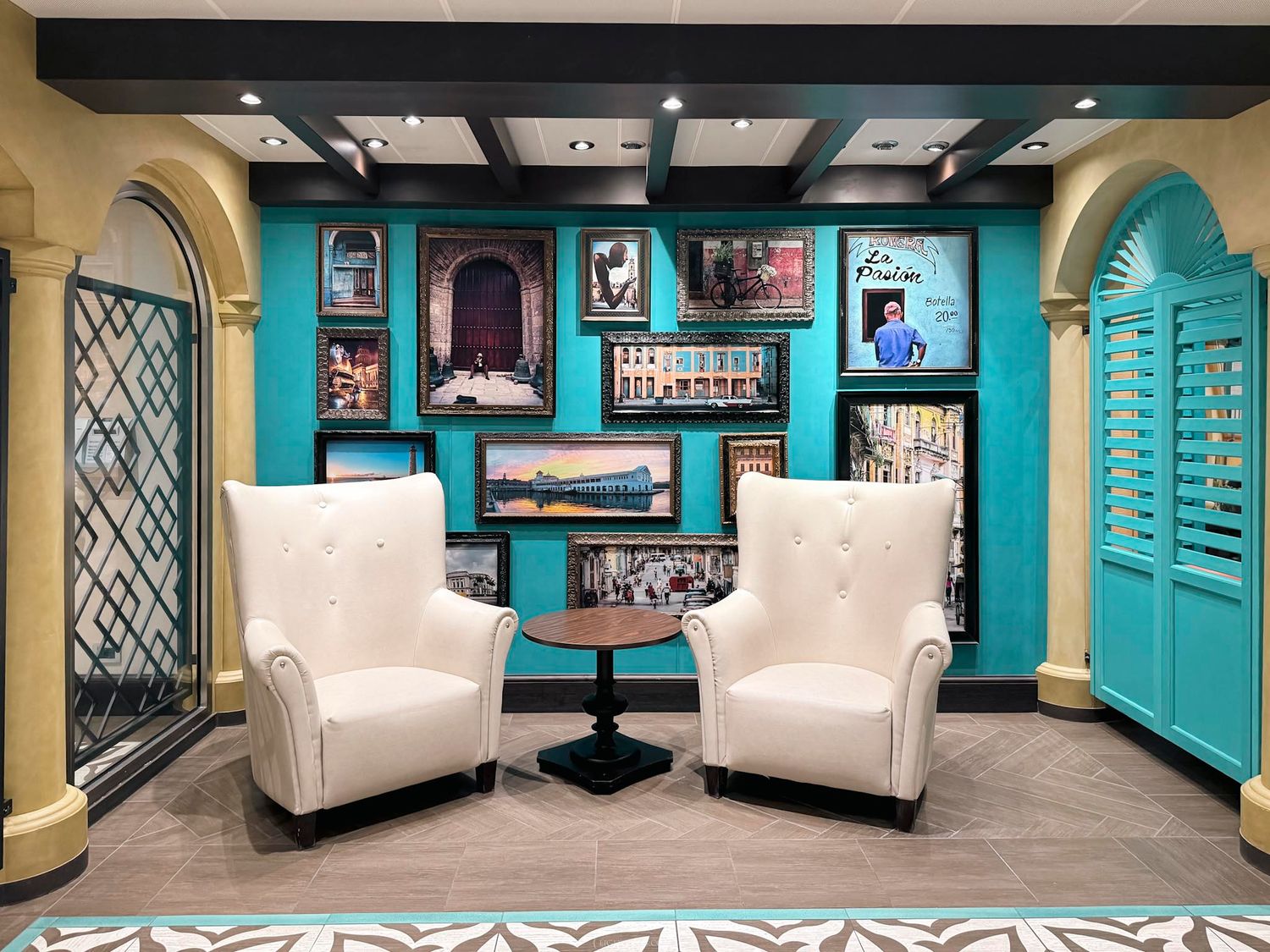 Elegant lounge area with teal walls, white armchairs, and colorful framed artwork display.