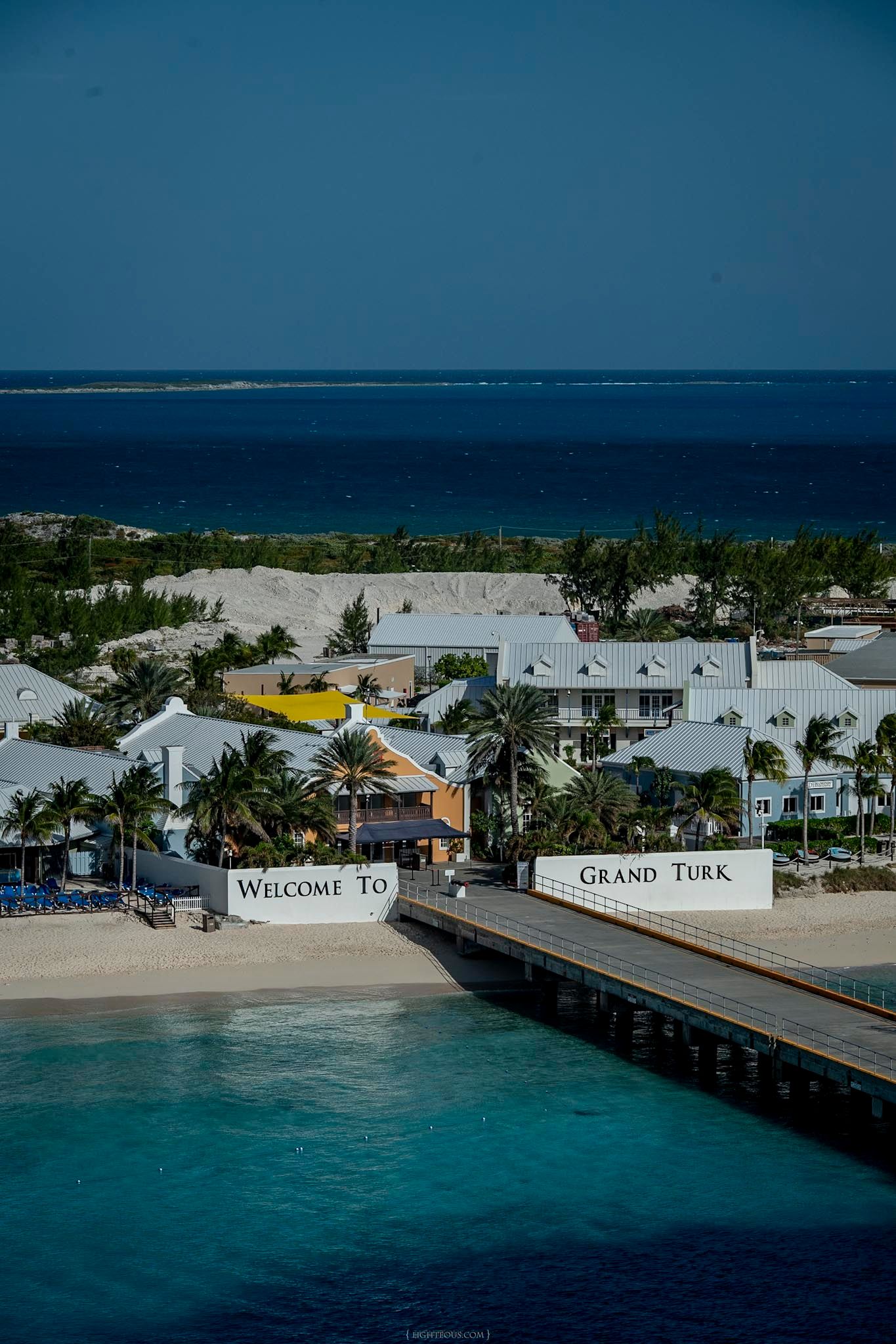 Aerial view of Welcome to Grand Turk sign near cruise pier with turquoise waters, palm trees, and colorful buildings.