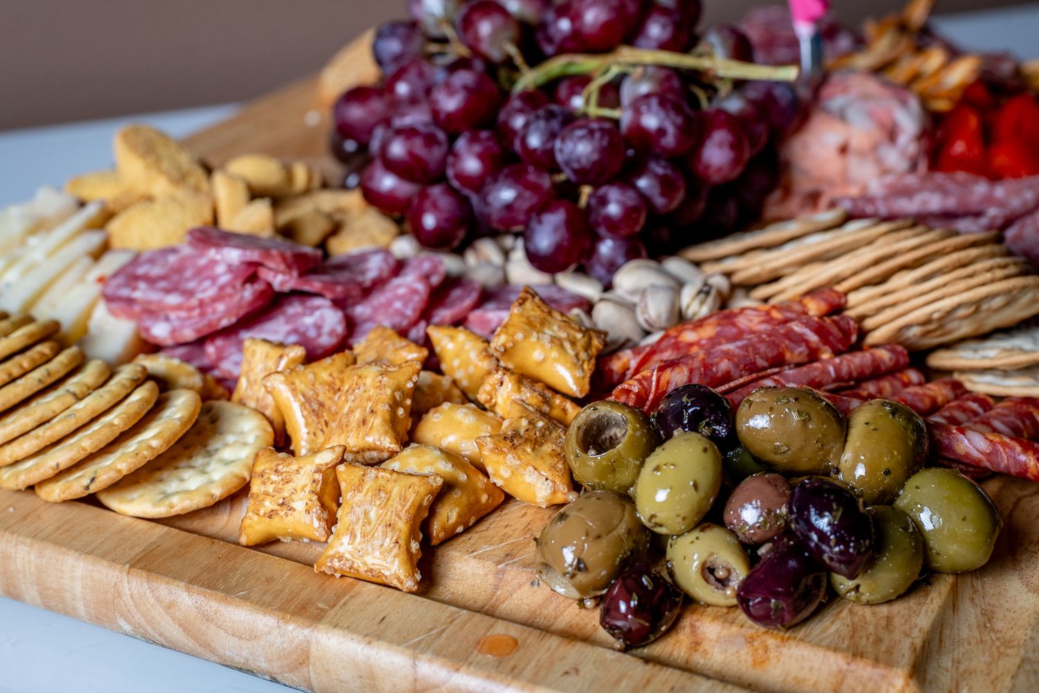 Charcuterie board with grapes, crackers, meats, olives and nuts arranged on wooden surface.