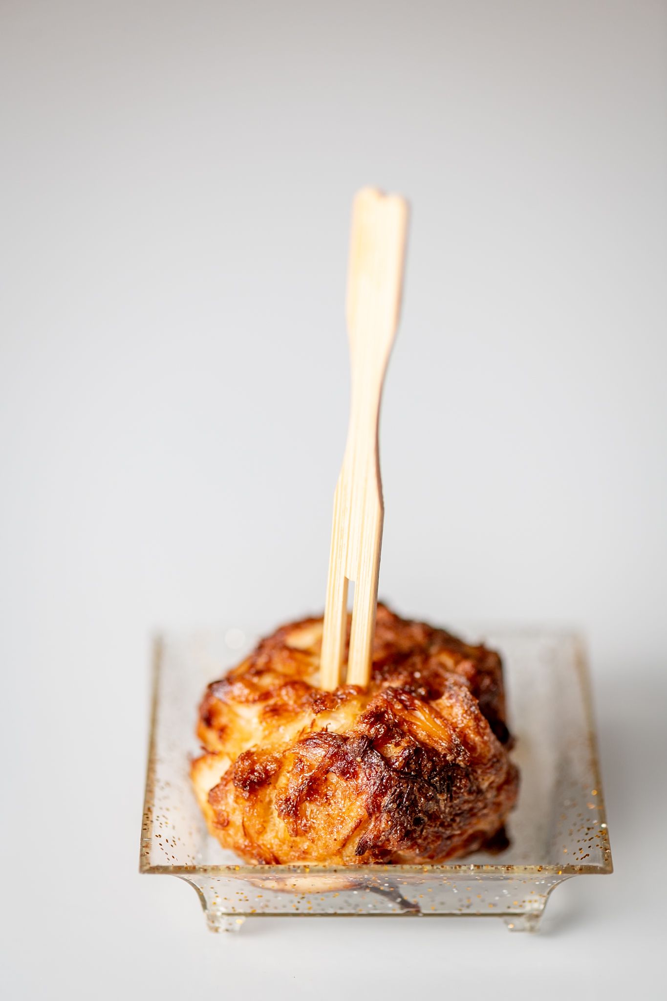 Crispy golden brown pastry with wooden skewer served on metallic plate.