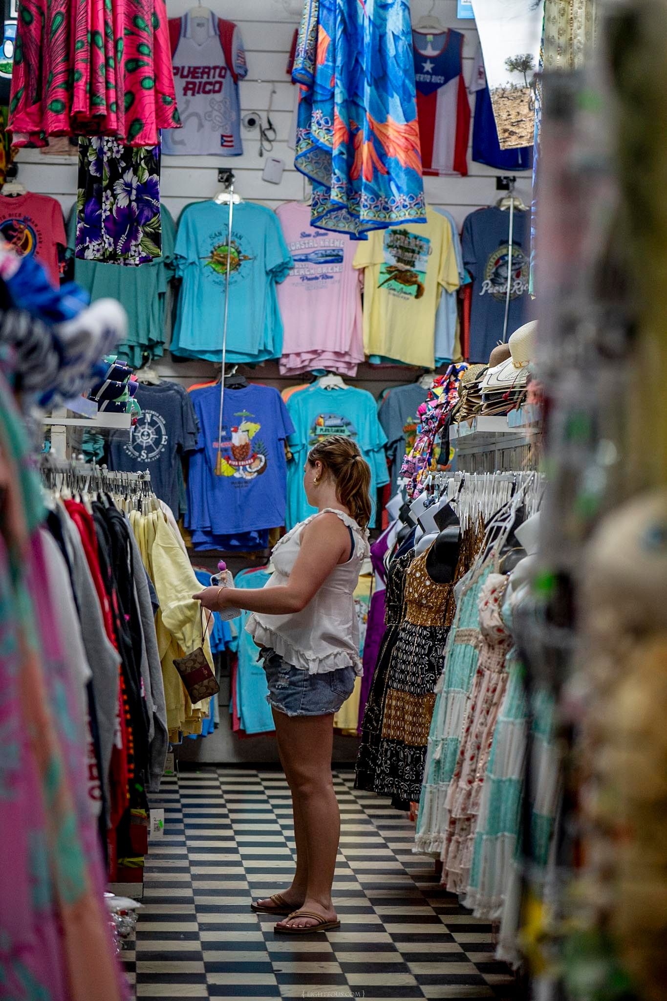 Woman browsing colorful Puerto Rico souvenir t-shirts and clothing in a vibrant tourist gift shop.
