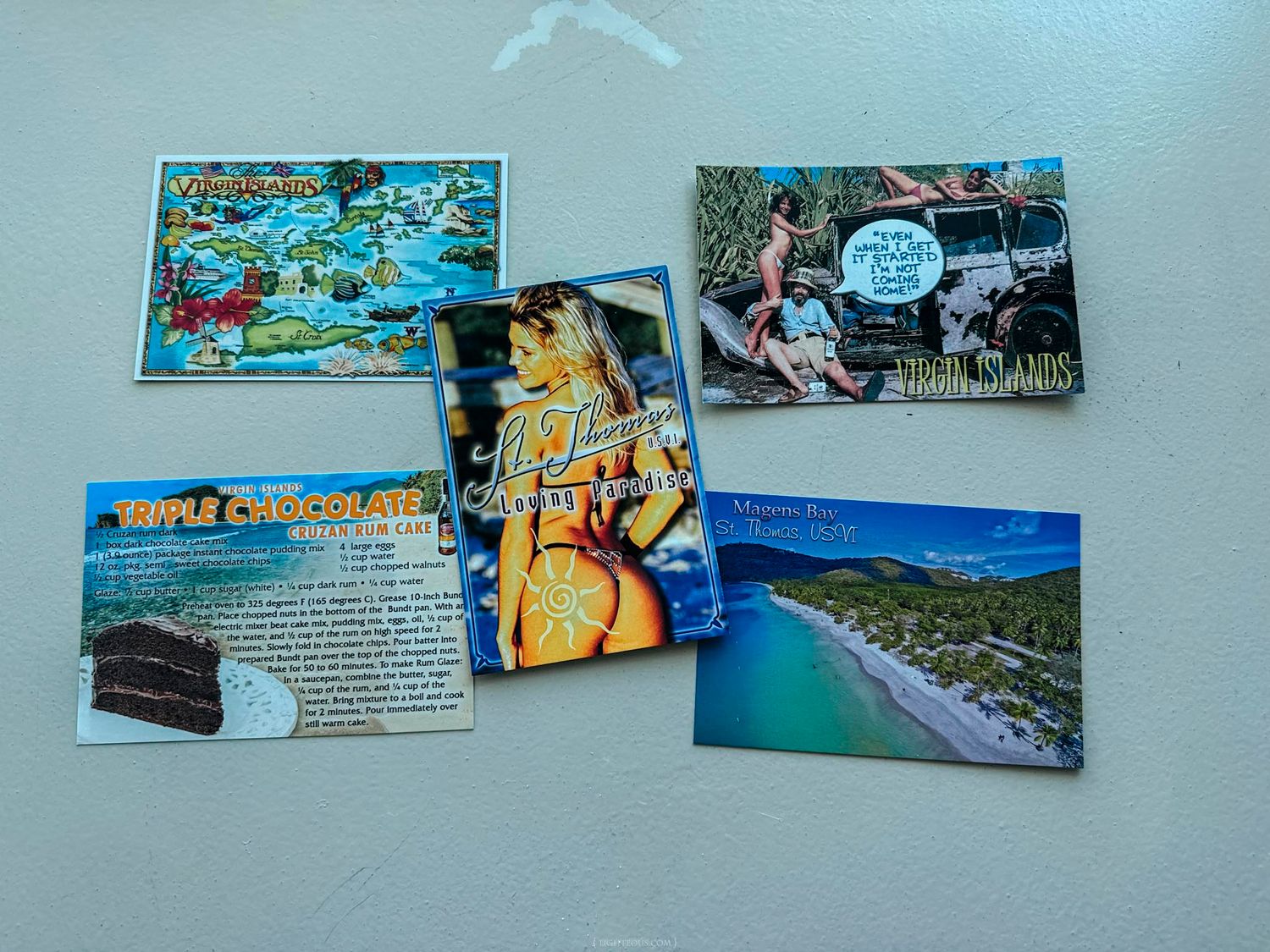 Five travel postcards displayed on a white surface featuring tropical destinations, a recipe card, and scenic beach and island views.