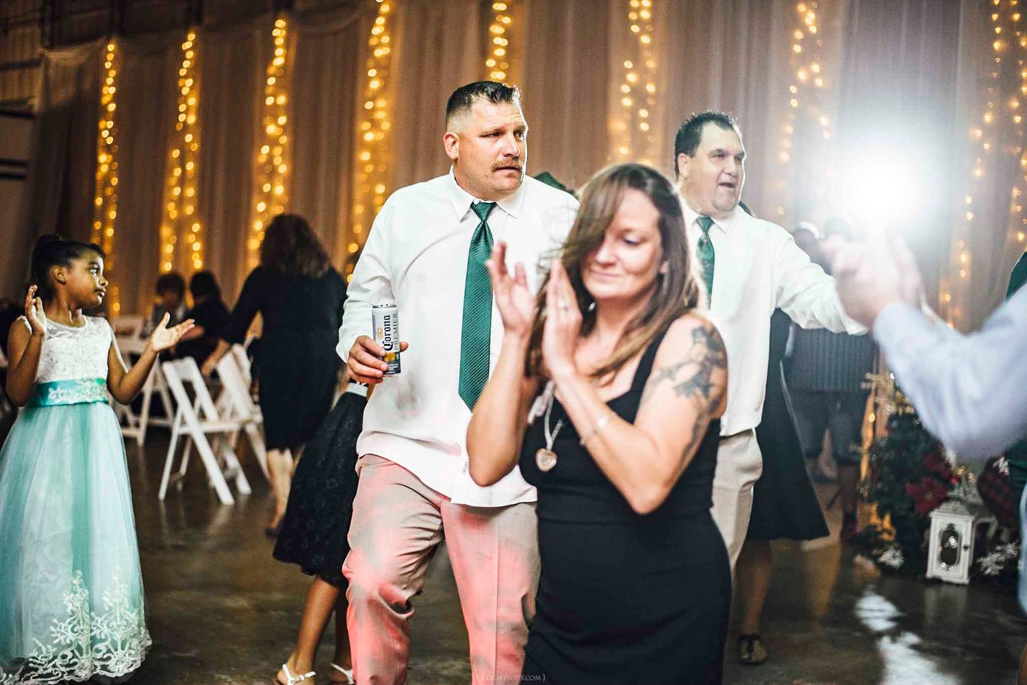 Guests dancing joyfully at a wedding reception with twinkling fairy lights in the background.