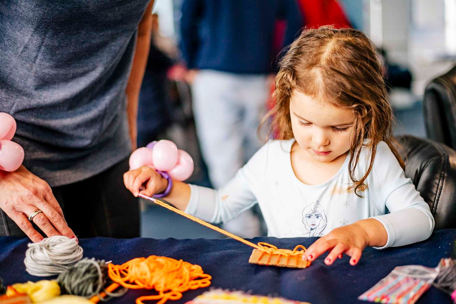Young girl doing a craft activity at a table with colorful yarn and materials.