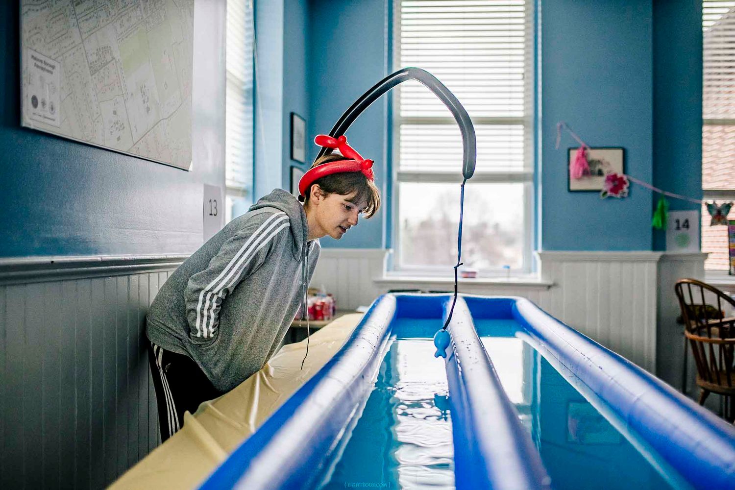 A student wearing a red hat examines a blue water channel experiment indoors.