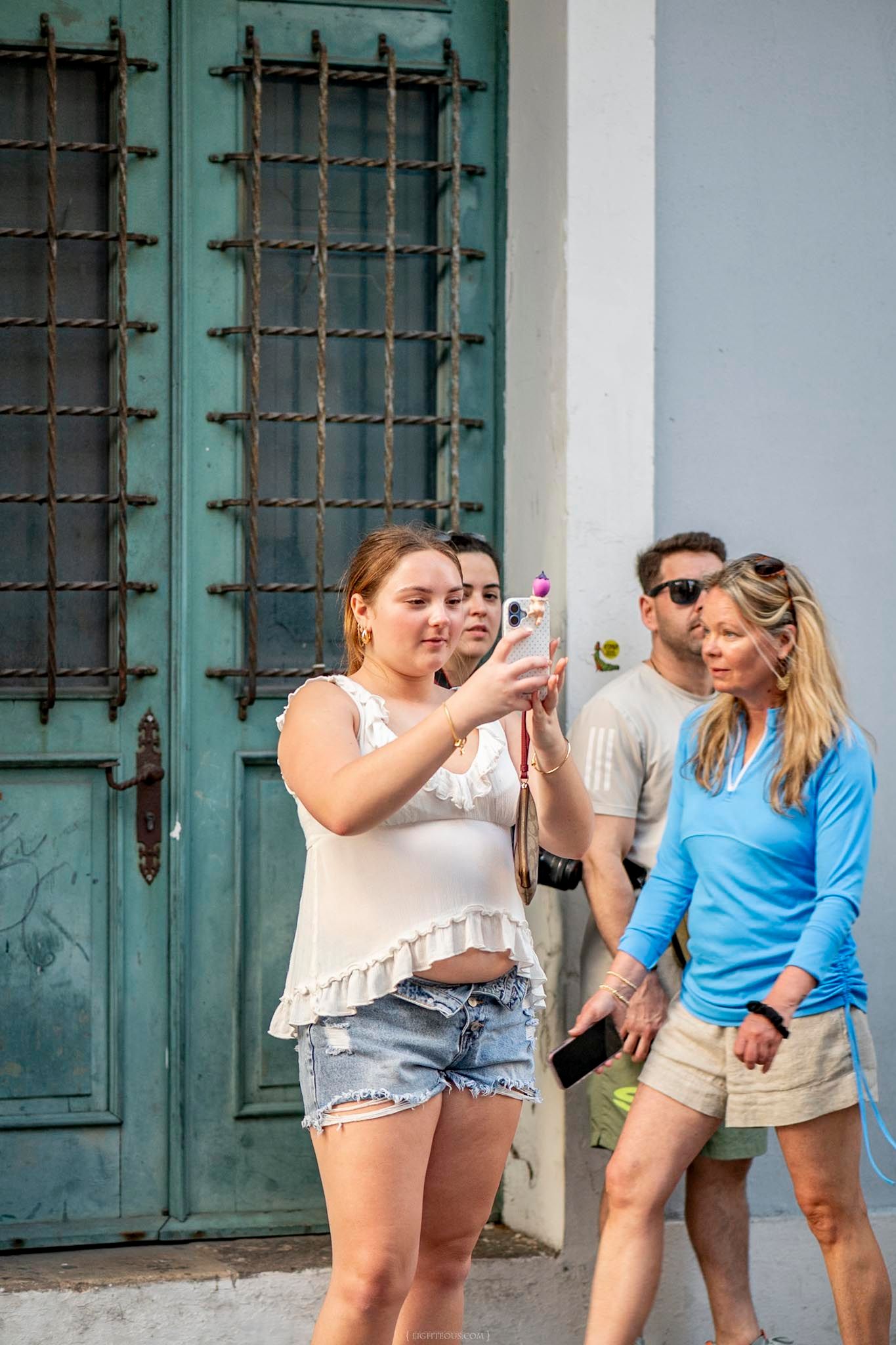 Tourists taking selfies outside a historic building with green doors in Old San Juan, Puerto Rico.