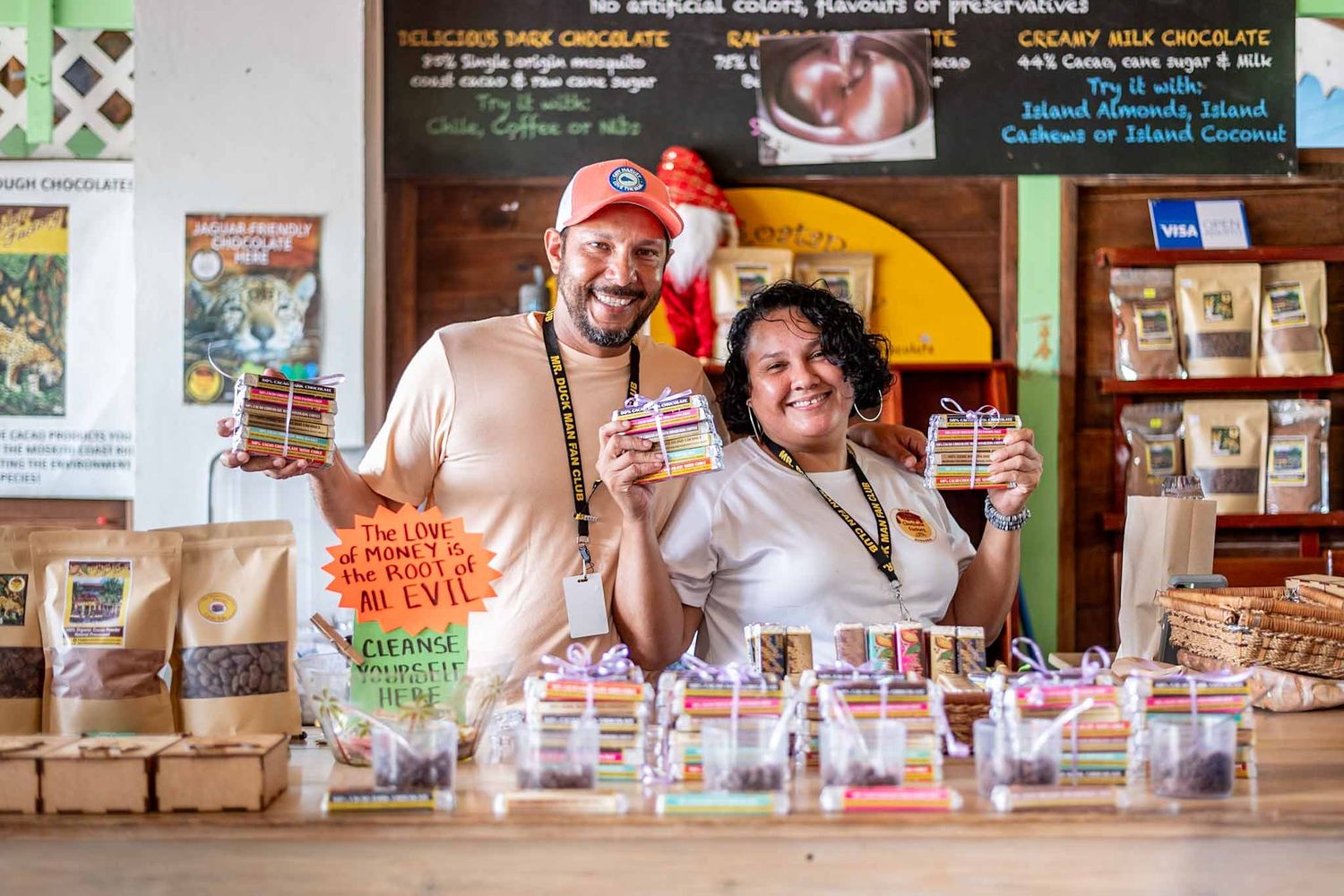 Two smiling employees stand behind the counter at a local coffee shop displaying their selection of products.