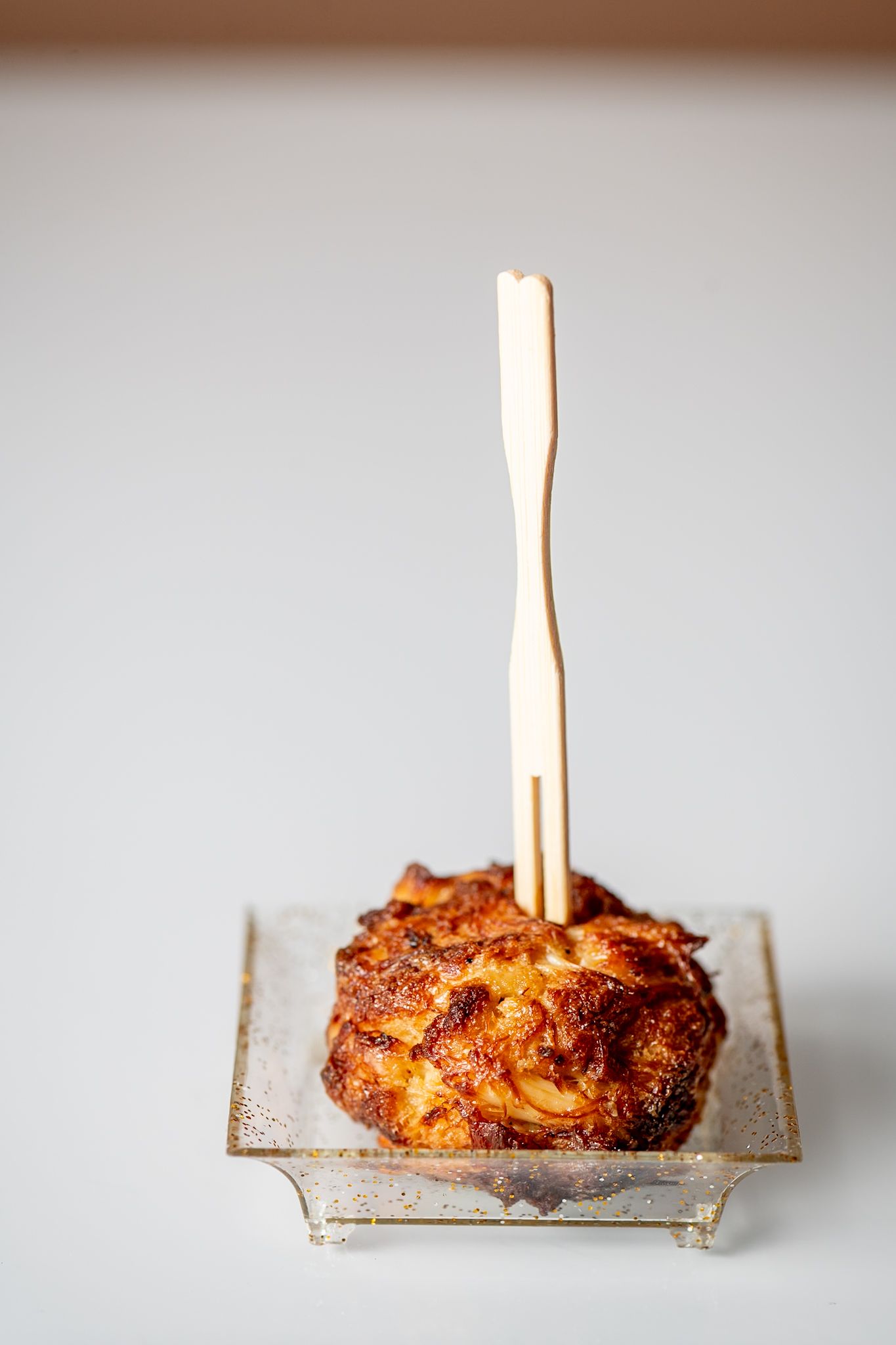 Golden brown pastry with a wooden skewer on a silver dish against light background.