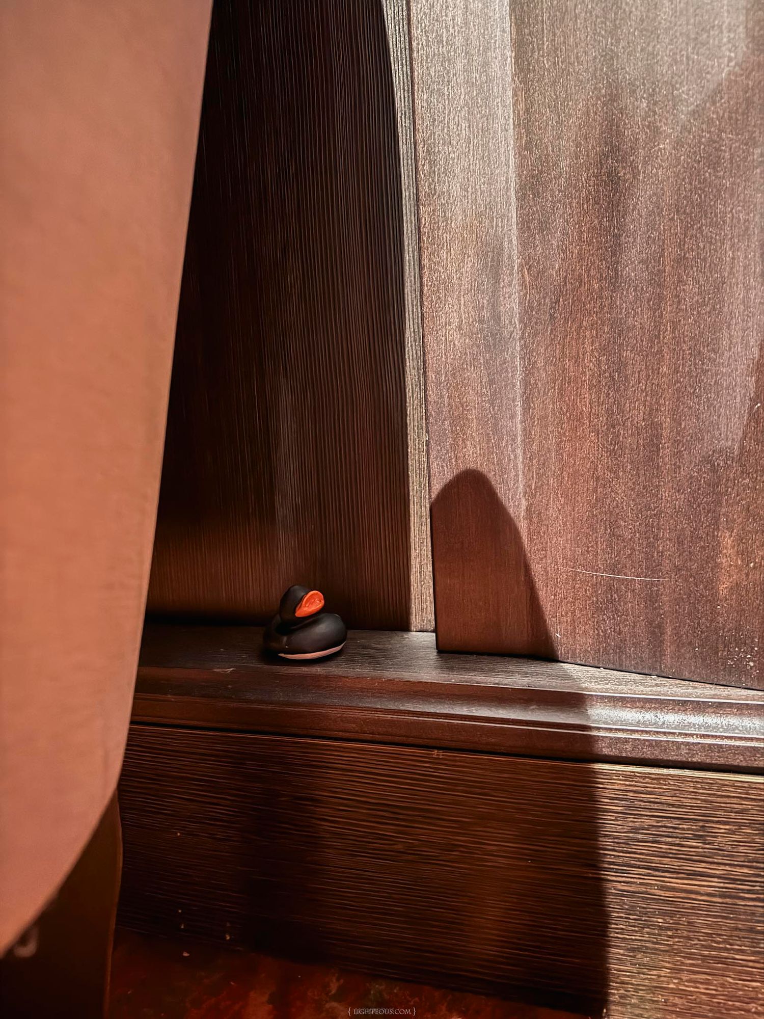 A small black door stopper with red accent sits at the base of a dark wooden cabinet door.