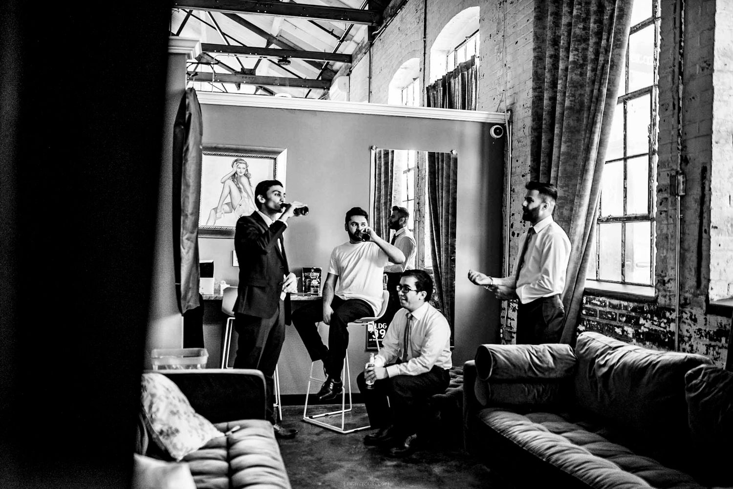 Black and white photo of groomsmen getting ready in a rustic loft space before a wedding ceremony.