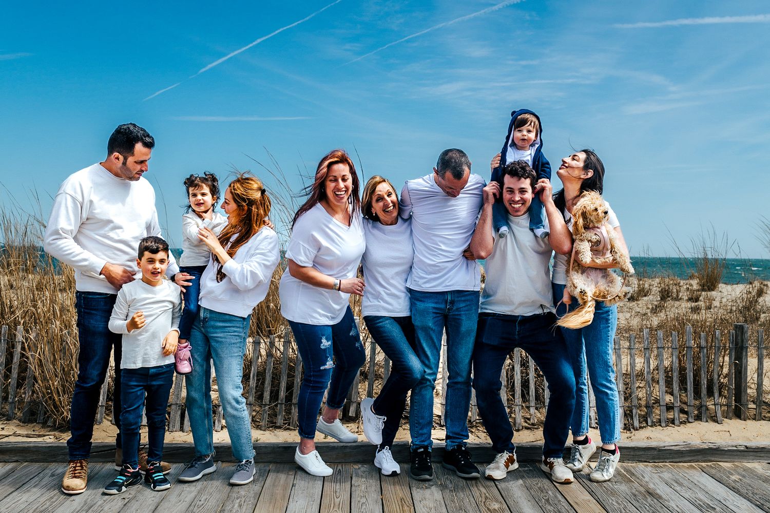 Happy family group in white shirts and jeans posing on a beach boardwalk on a sunny day.
