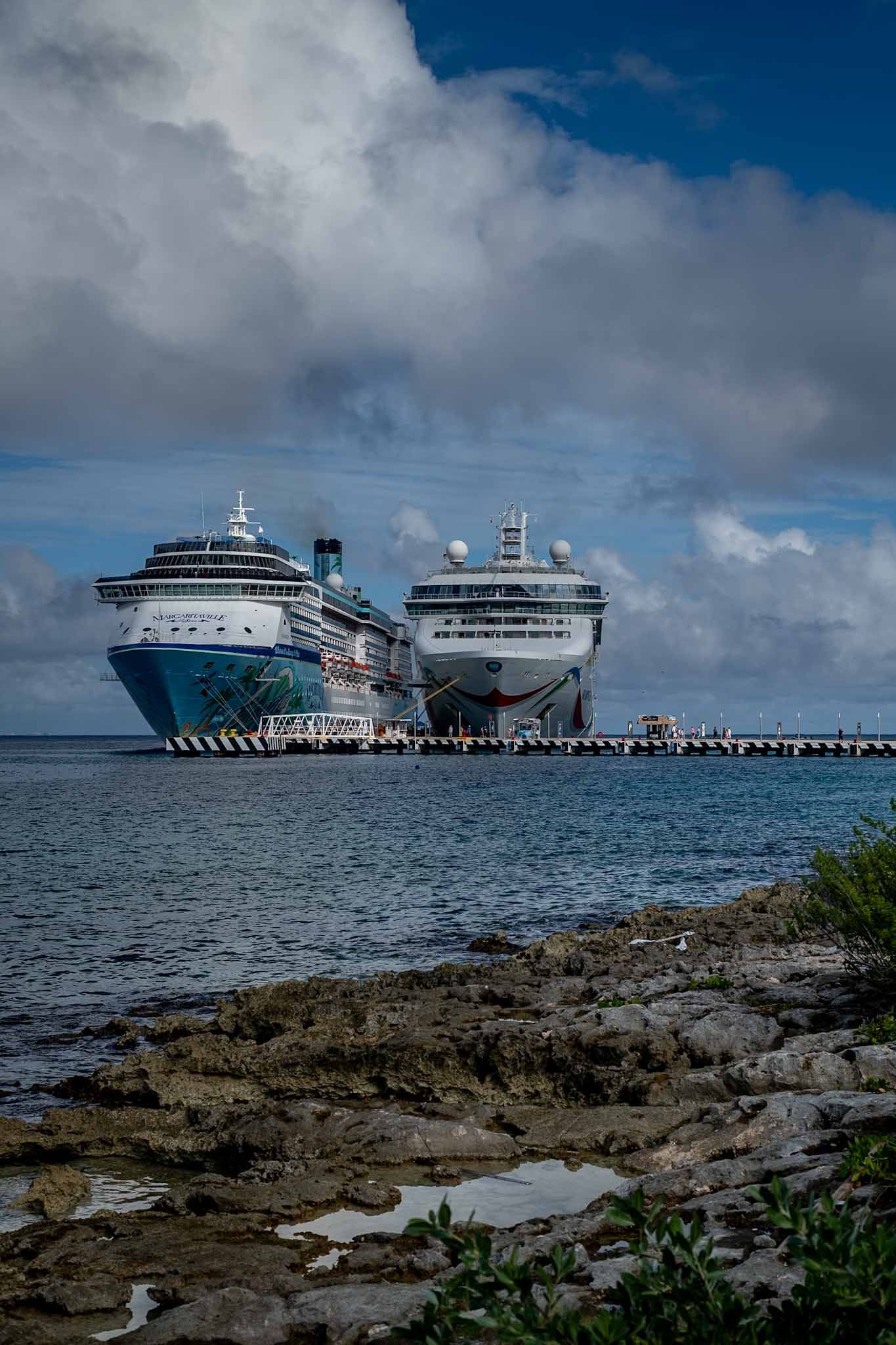 Three large cruise ships docked in tropical waters under partly cloudy skies.