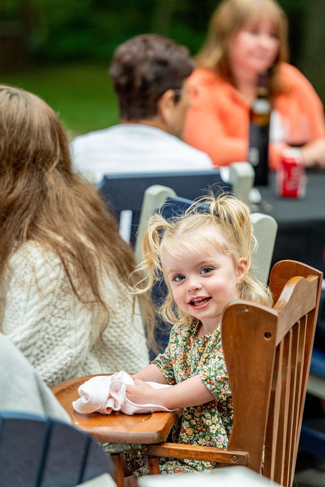 A young guest enjoying themselves at an outdoor dinner party while seated in a wooden chair.