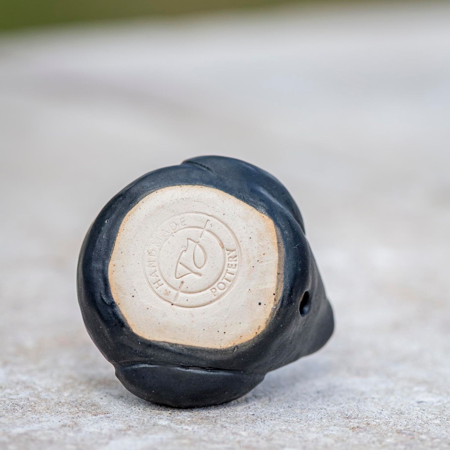 Bottom view of a black glazed ceramic duck showing maker's mark stamp on unglazed base.