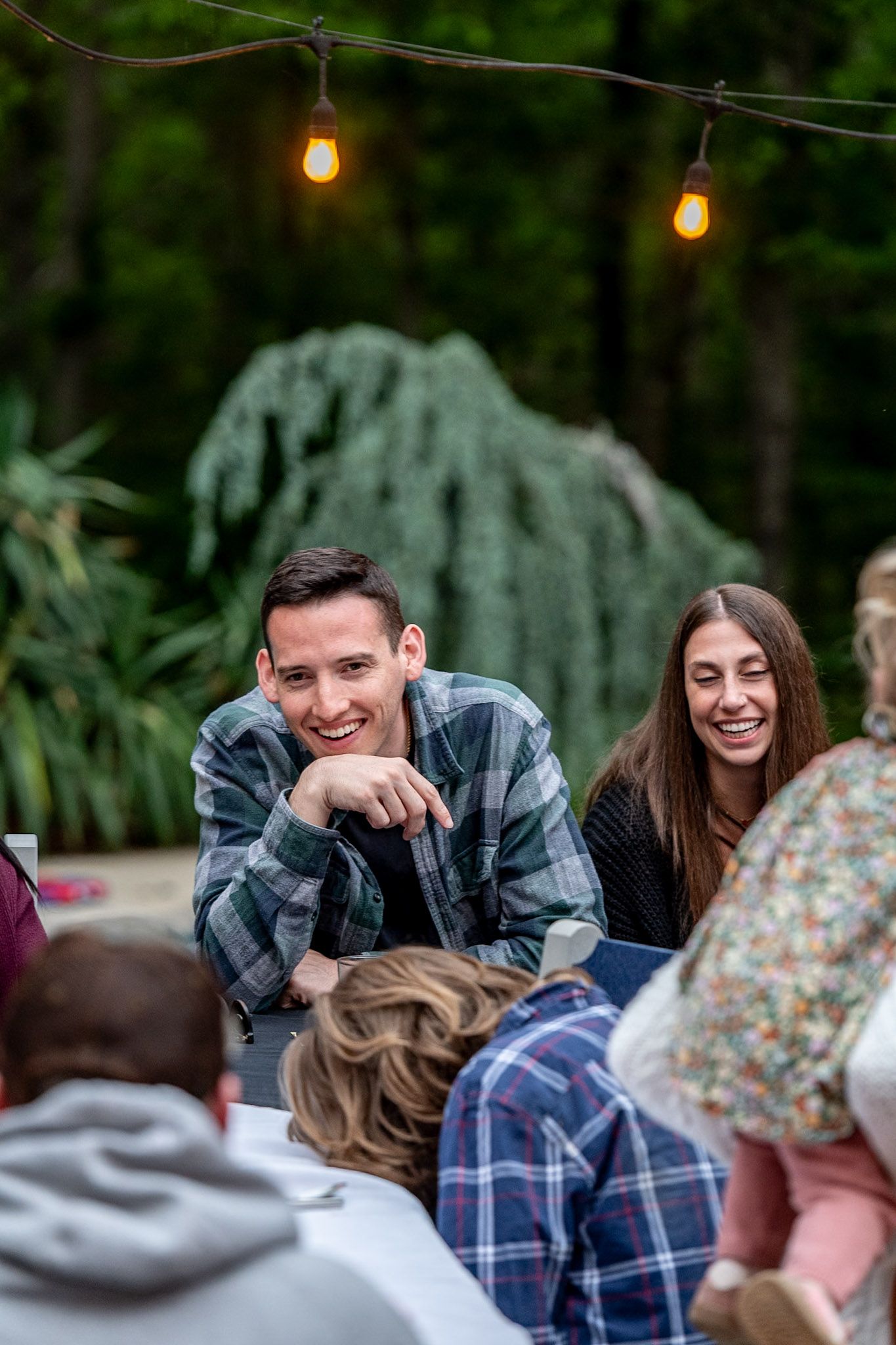 Guests sharing laughter and conversation at outdoor tables during an evening gathering.