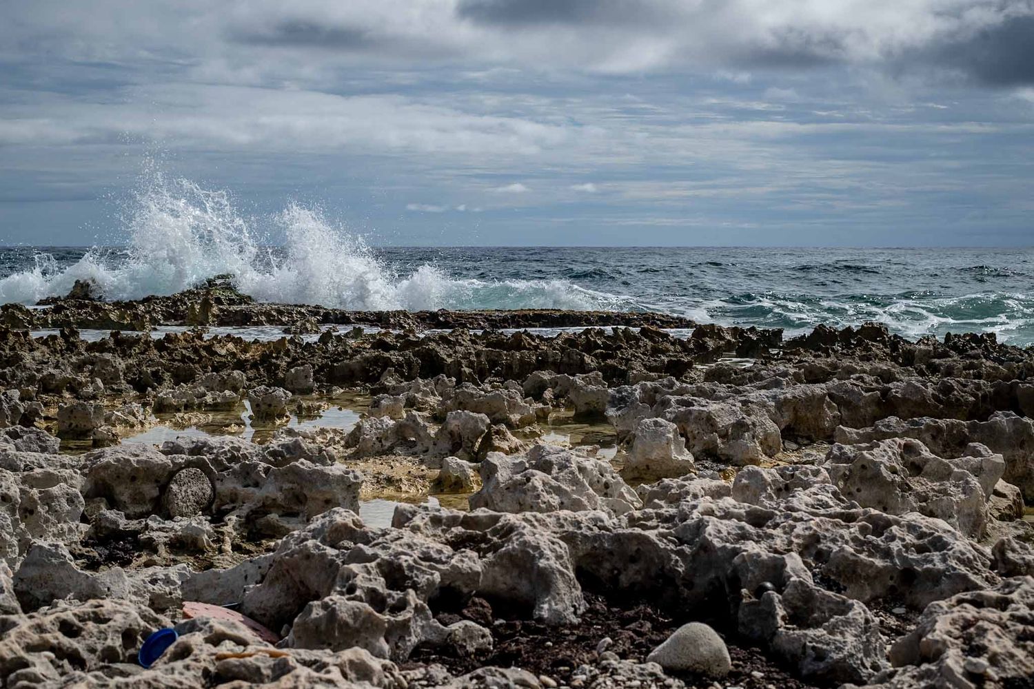 Rocky coastal shoreline with crashing waves and dramatic cloudy sky overhead.