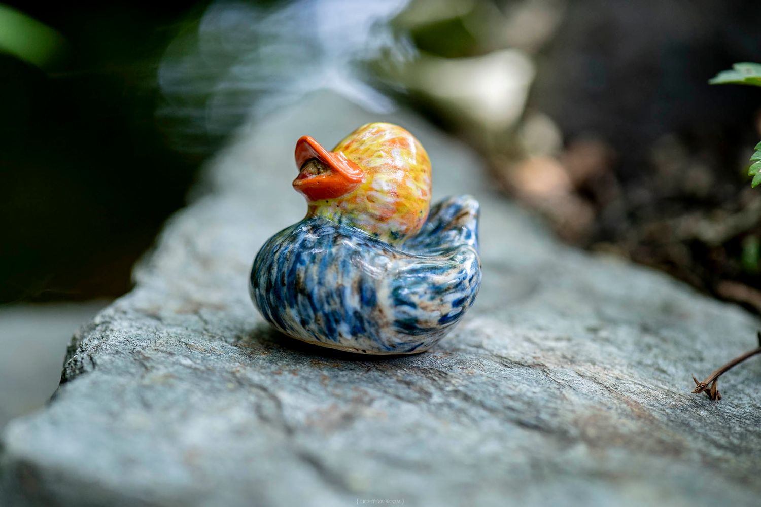 Colorful blue and orange swirled glass duck figurine sitting on a gray stone surface.
