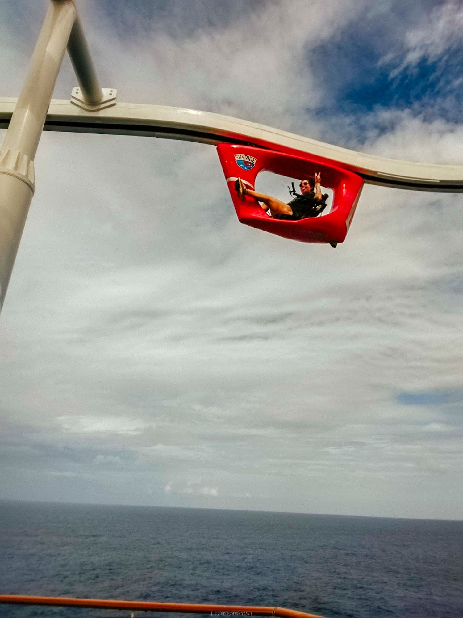 A person rides a red suspended roller coaster pod over the ocean on a cruise ship.