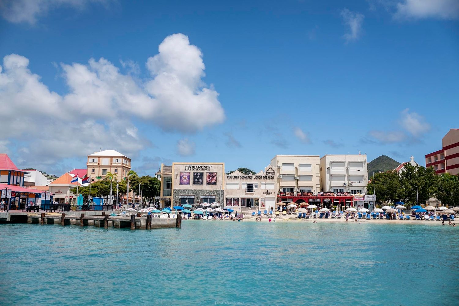 A vibrant waterfront shopping district with colorful buildings viewed from turquoise Caribbean waters.