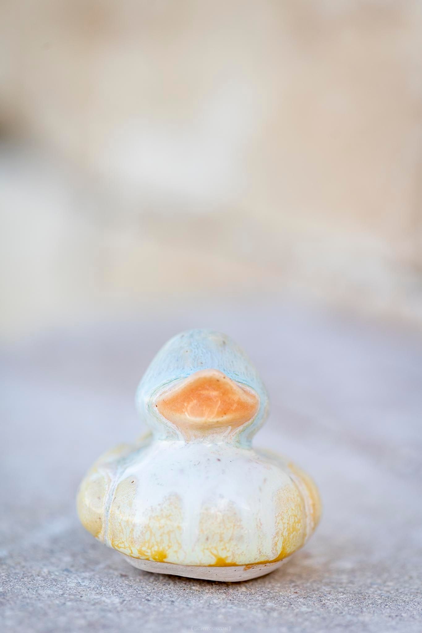 Weathered ceramic rubber duck figurine with blue and yellow paint on a stone surface.