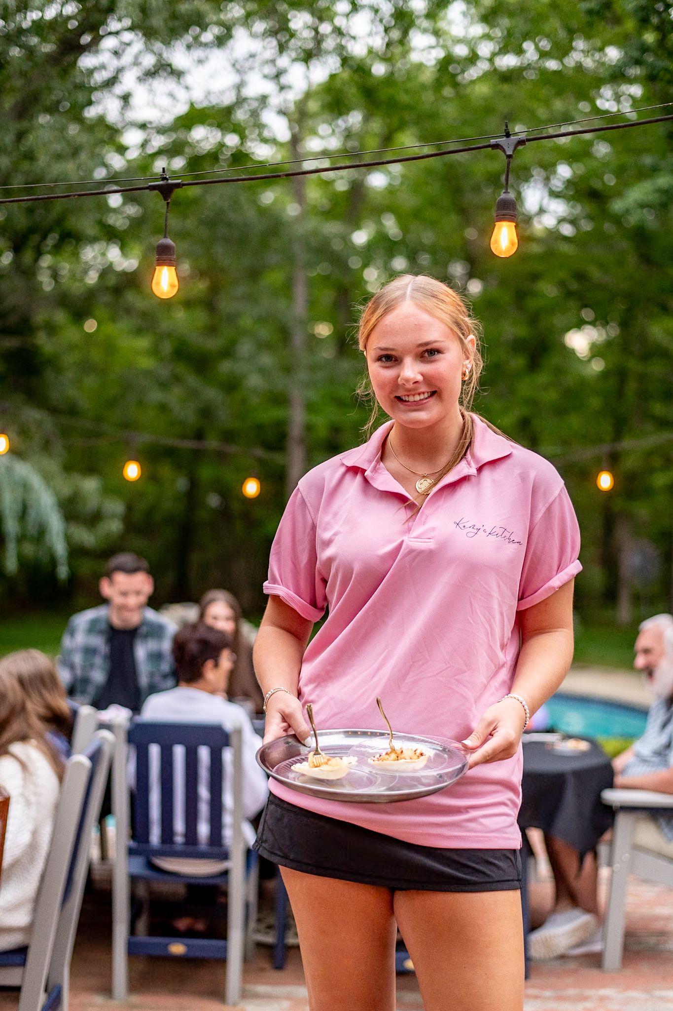Outdoor dining scene with string lights where someone serves food on a summer evening.