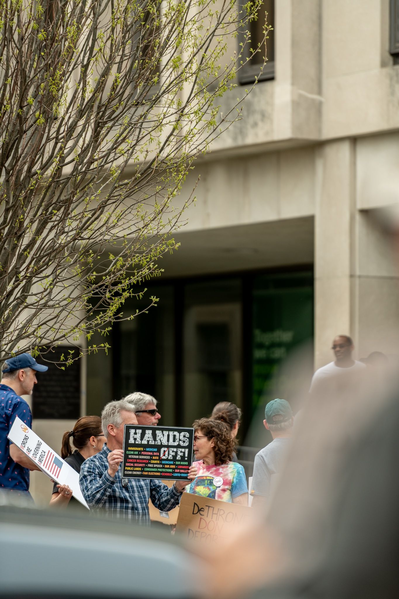 Crowd holds protest signs during a demonstration outside a modern building structure.