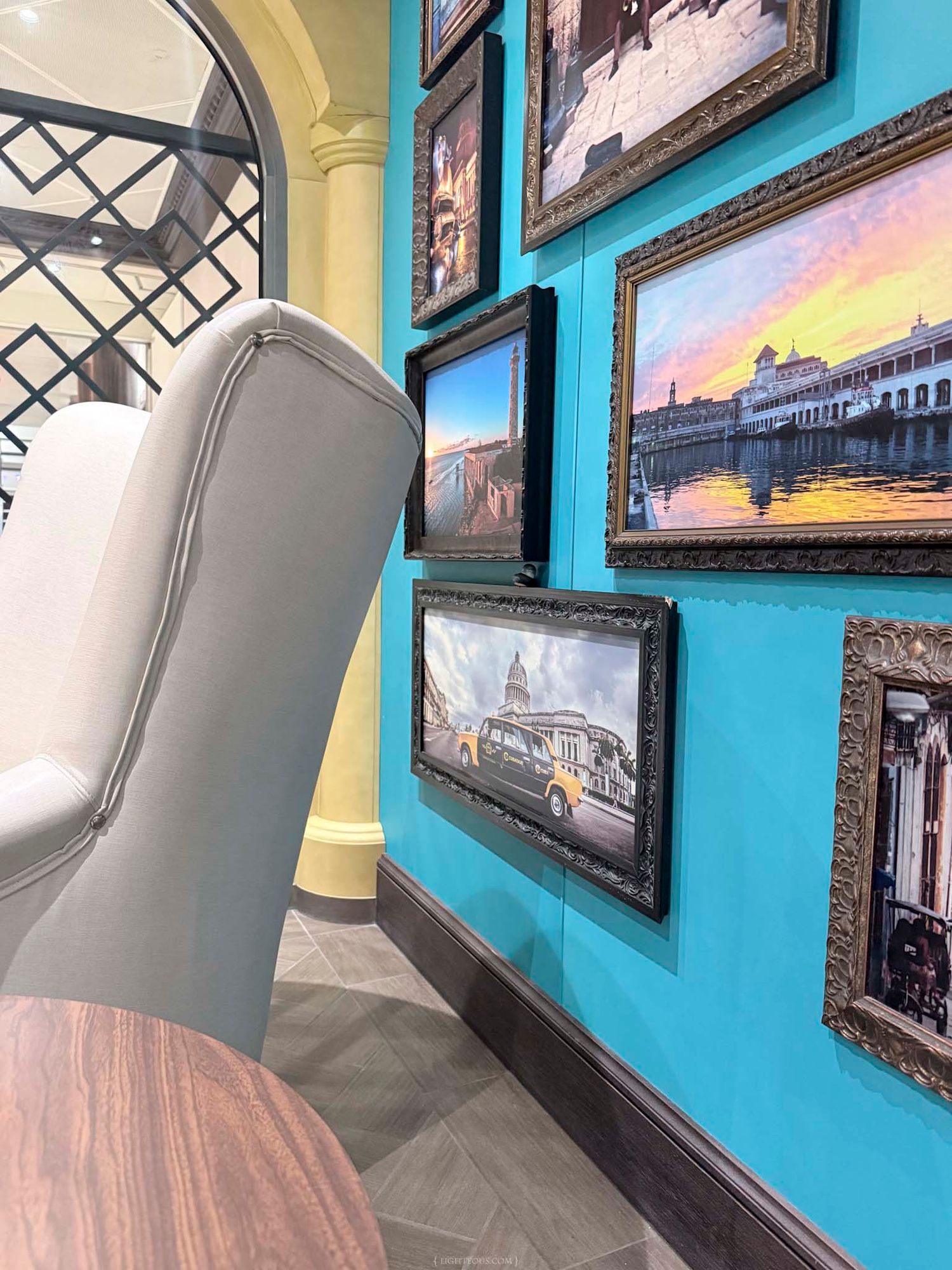 Turquoise restaurant wall adorned with ornate framed travel photos, modern white chair, and warm wood table in stylish interior.