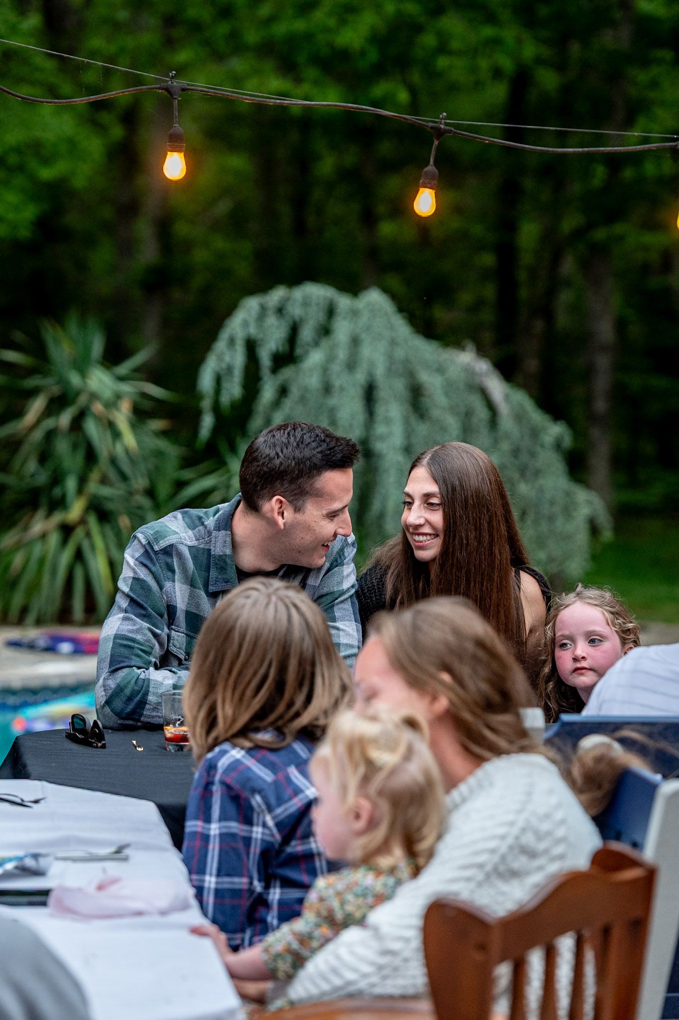 Friends gathered around outdoor tables for a casual evening get-together under string lights.