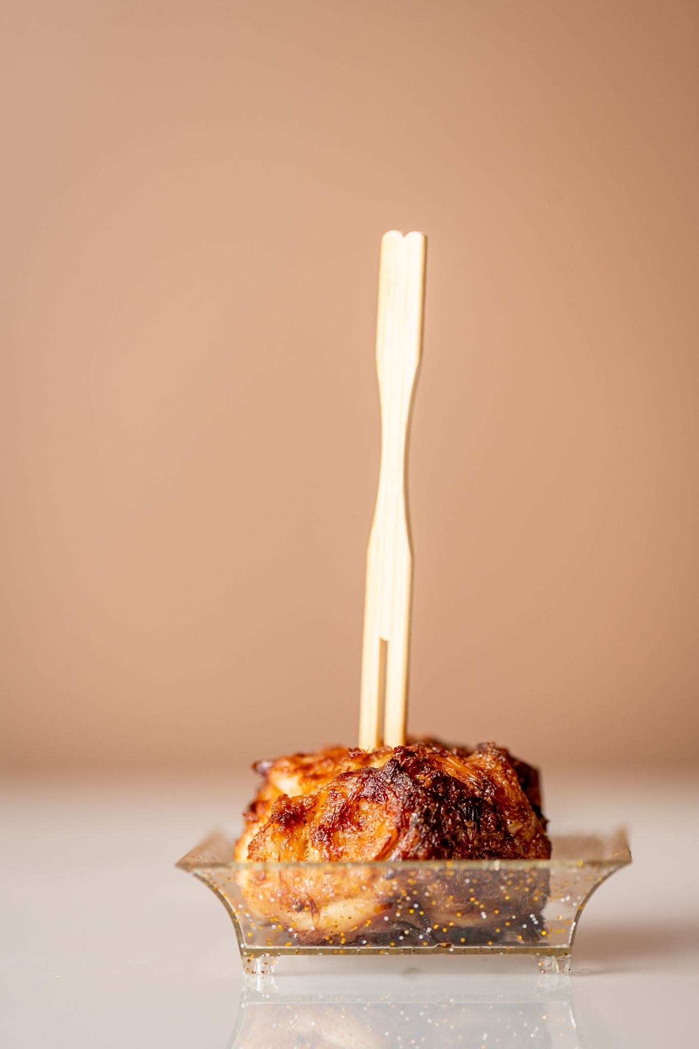 Grilled meat with caramelized edges served on a clear glass dish against a warm brown background.