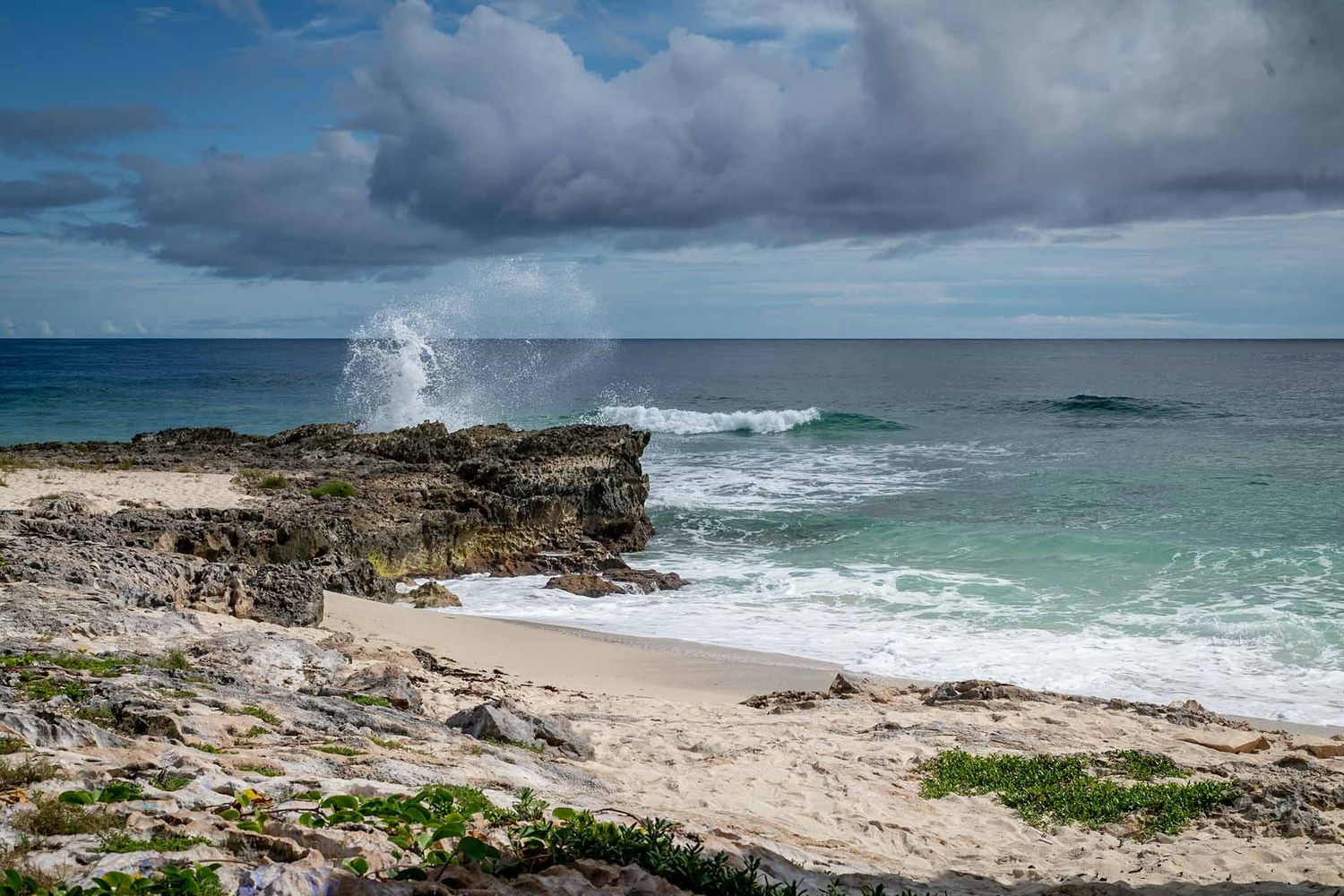 Dramatic coastal landscape with crashing waves against rocky cliffs under a cloudy sky at a tropical beach location.