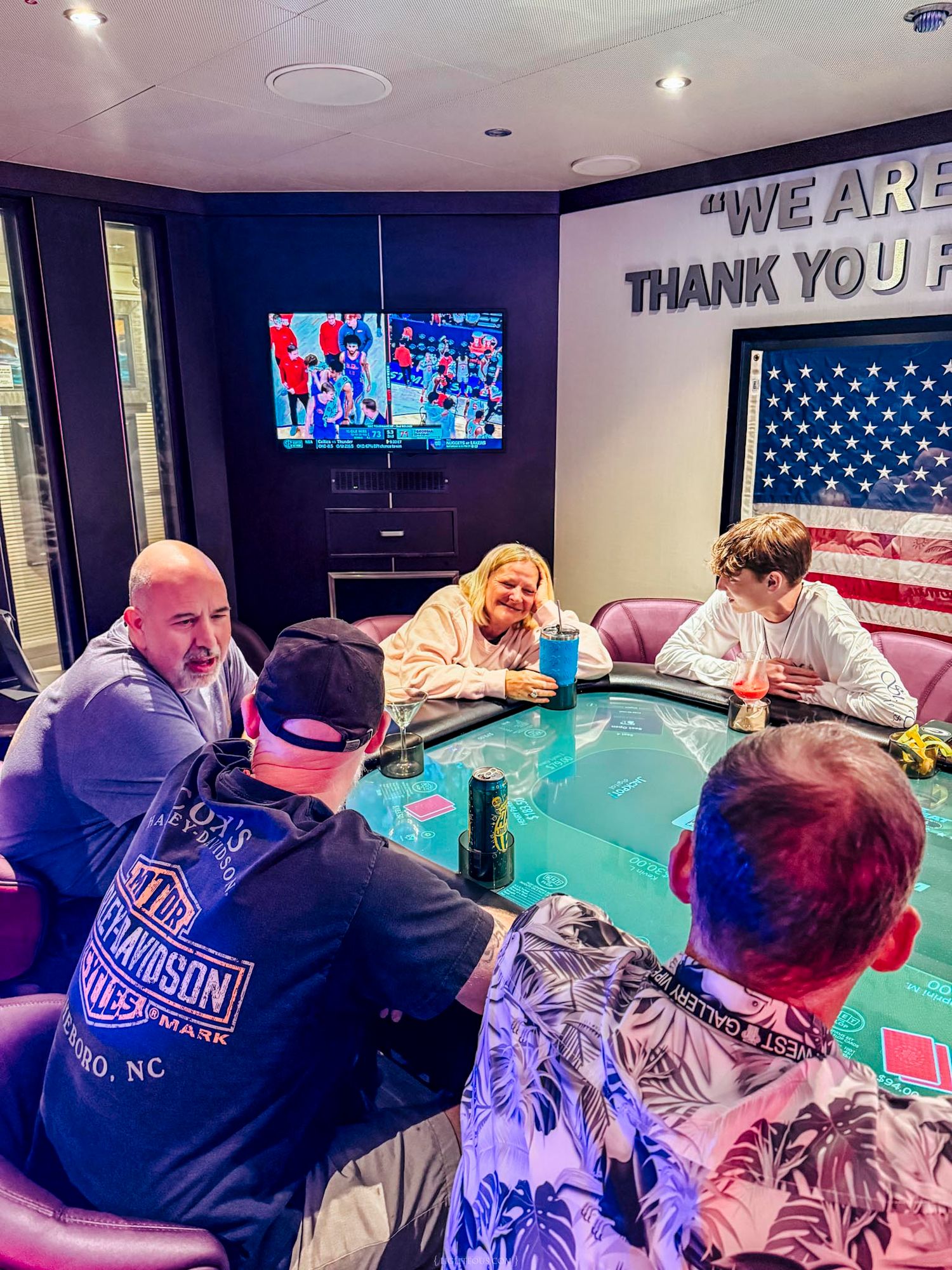 Group of friends playing poker around a round table with TV and American flag in a private game room.