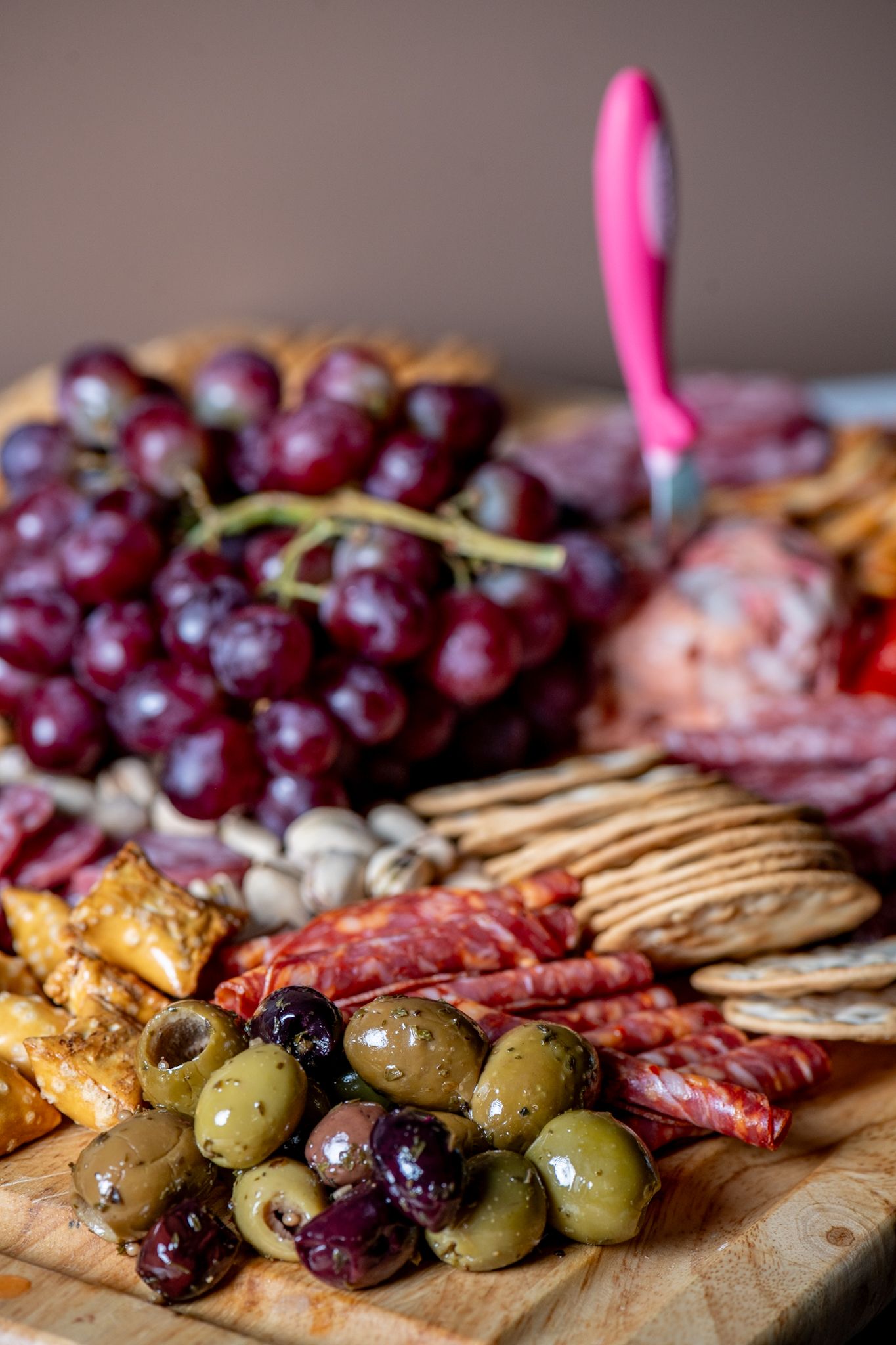 Charcuterie board with grapes, olives, crackers and cured meats arranged on wooden surface.