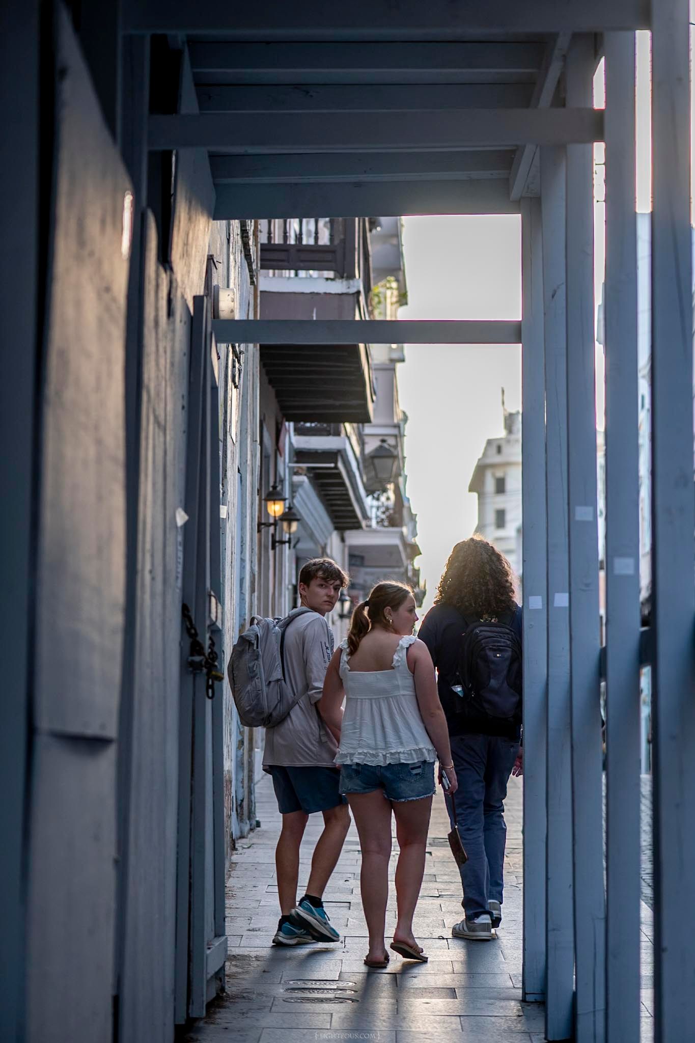 Three tourists walk through a narrow alleyway passage in New Orleans French Quarter at golden hour sunset.