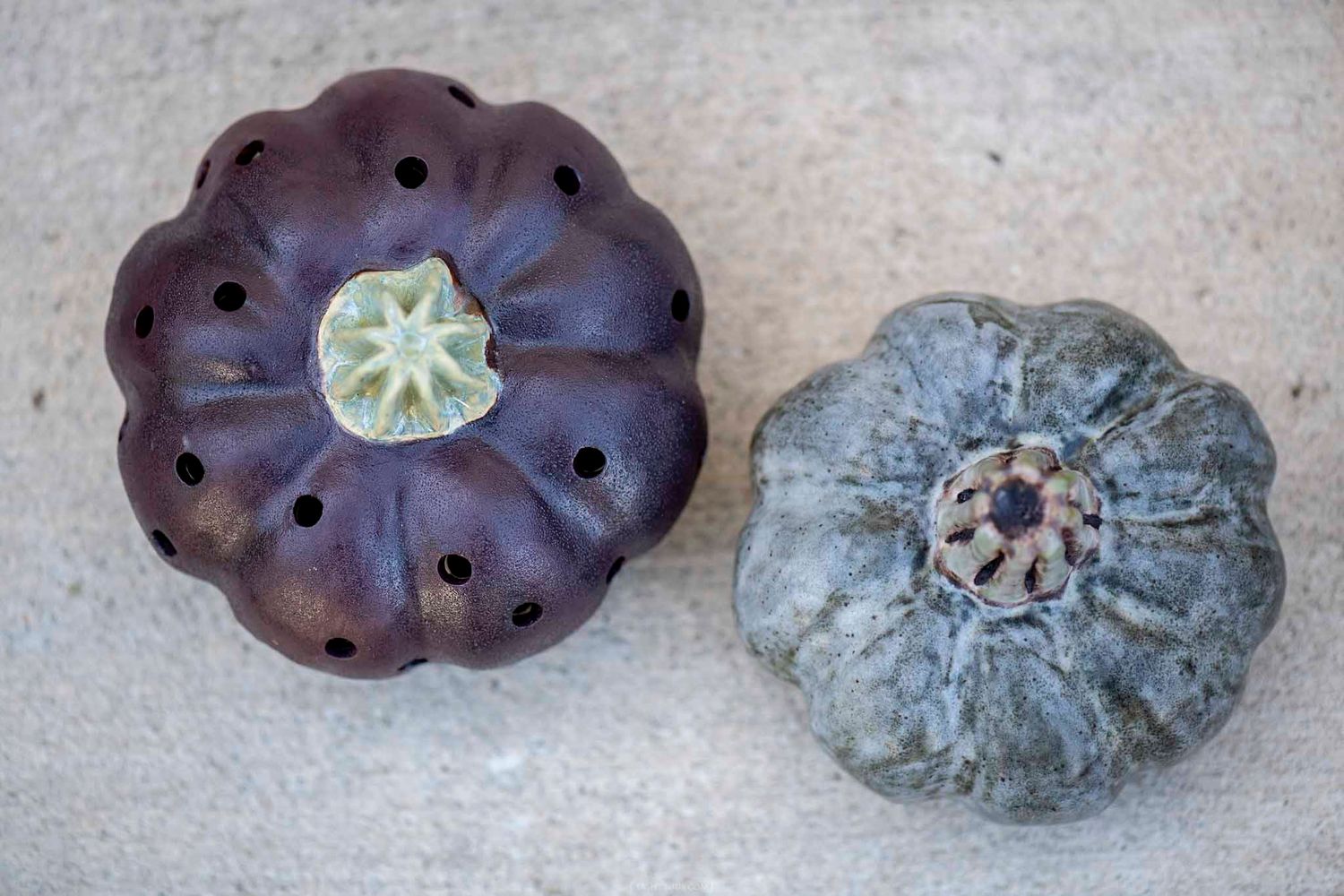 Two decorative dark purple and gray pumpkins with unique hole patterns on a concrete surface.