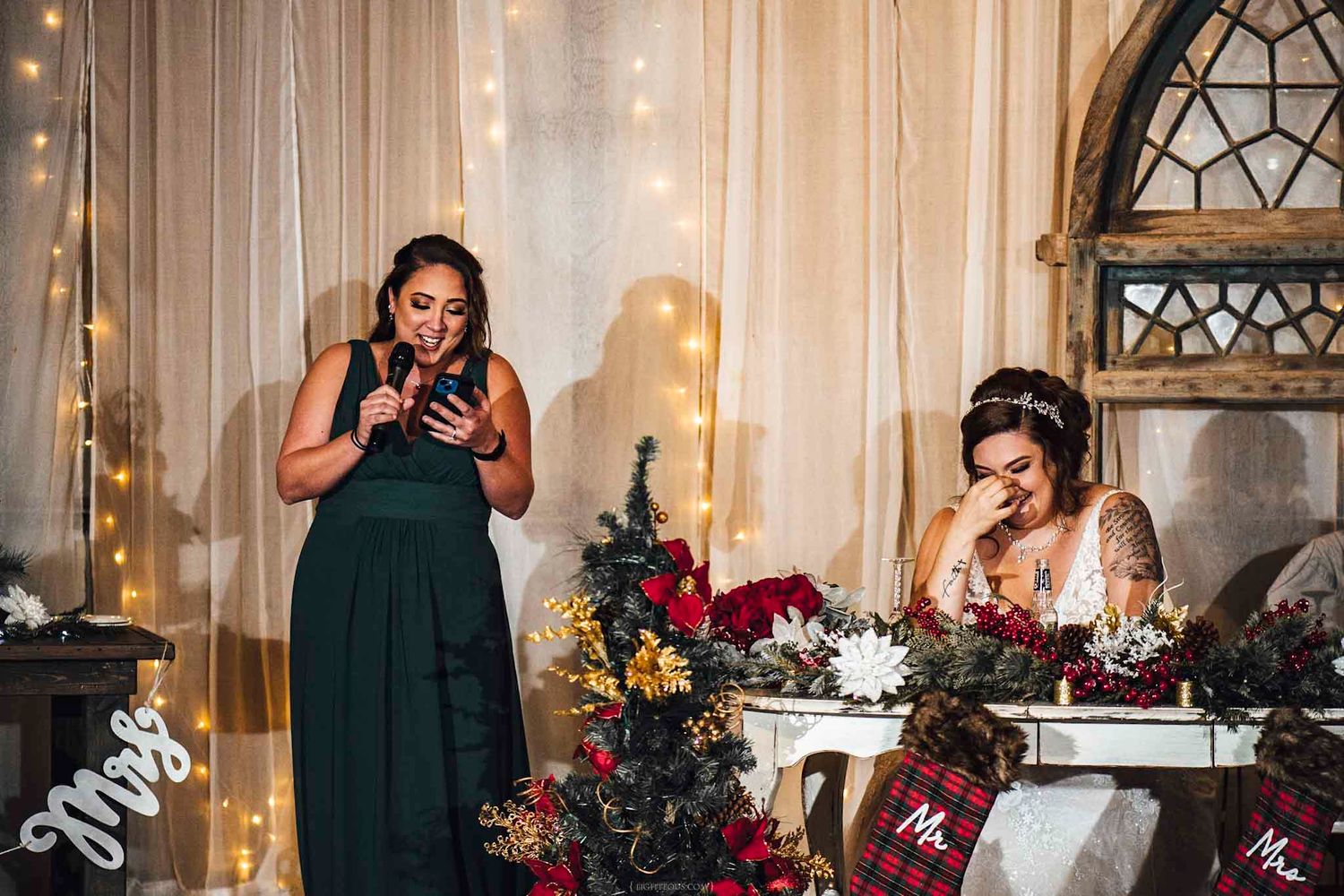 Bridesmaid in green dress reads speech while emotional bride laughs at Christmas wedding reception.