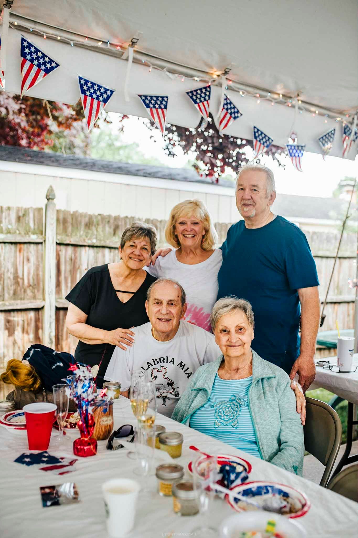 Group of five seniors celebrating Fourth of July under a tent decorated with American flags and bunting.