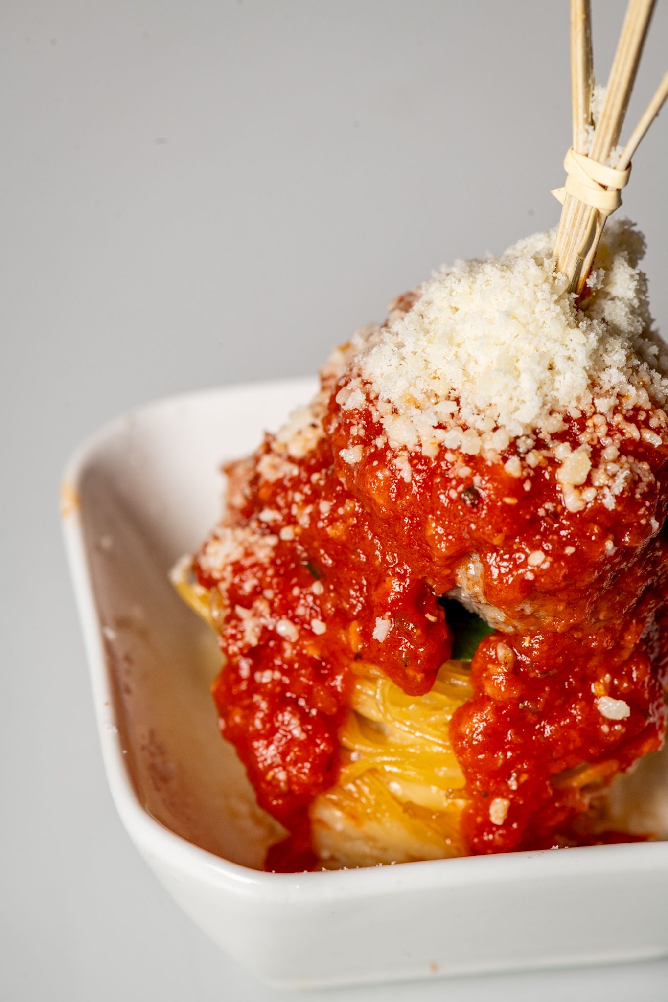 Red sauce and parmesan topped appetizer with wooden chopsticks in a white dish.