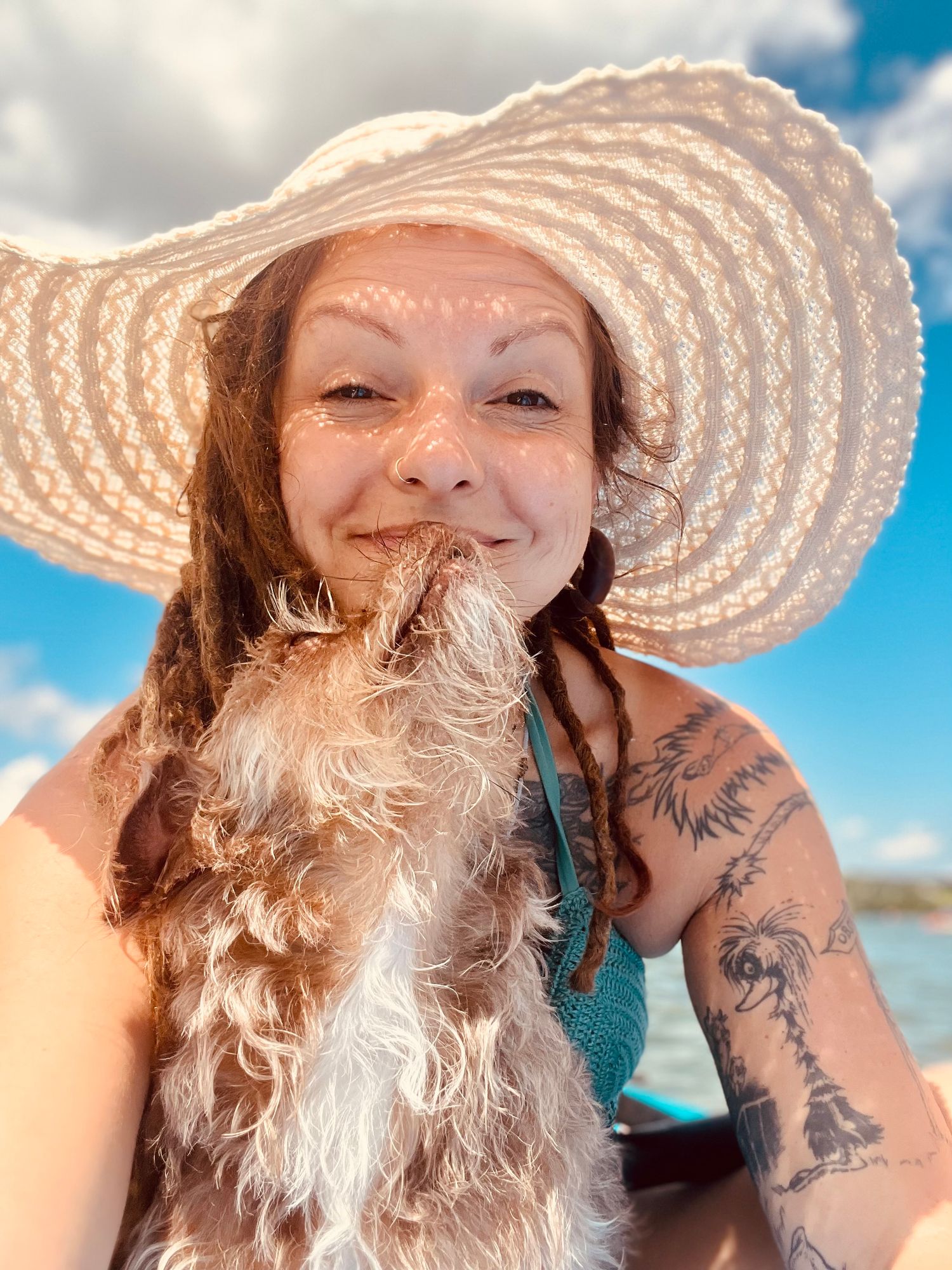 Tiffanie Quinn in wide-brim sun hat holds a fluffy dog close to her face at the beach.