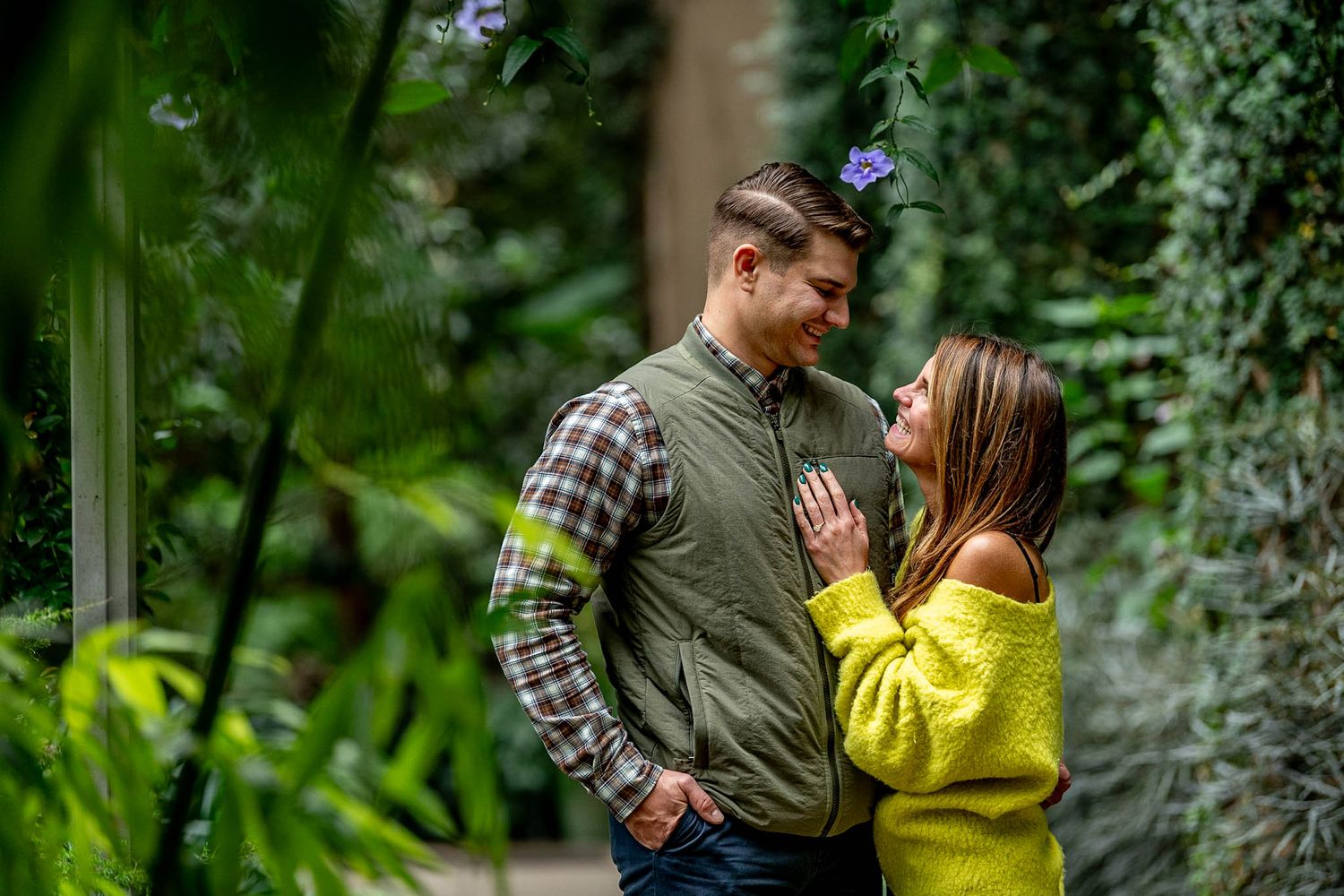 Couple sharing a romantic moment surrounded by lush green plants in a botanical garden setting.
