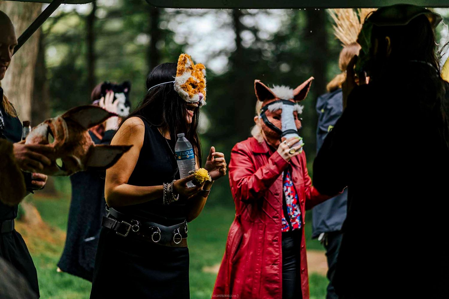 People wearing animal masks socialize outdoors at a costume party in a forest setting.