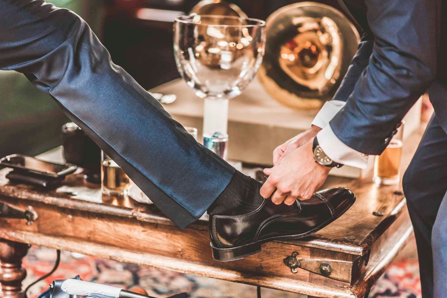 A man in a suit getting his black dress shoes fitted by another person in formal attire.