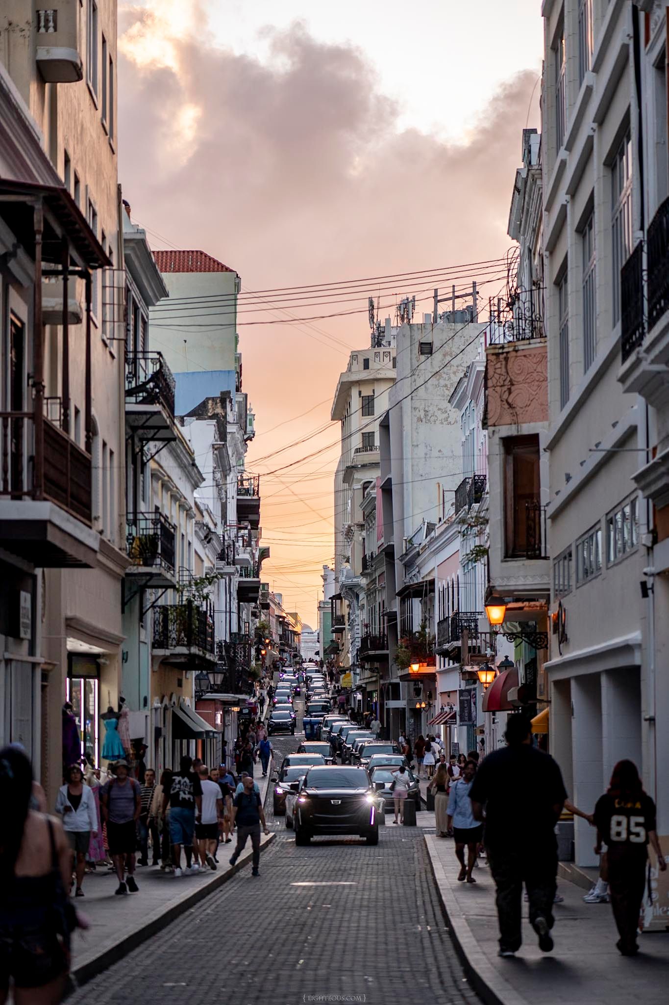 Busy urban street at sunset with pedestrians and cars flanked by colorful colonial buildings in Old San Juan, Puerto Rico.