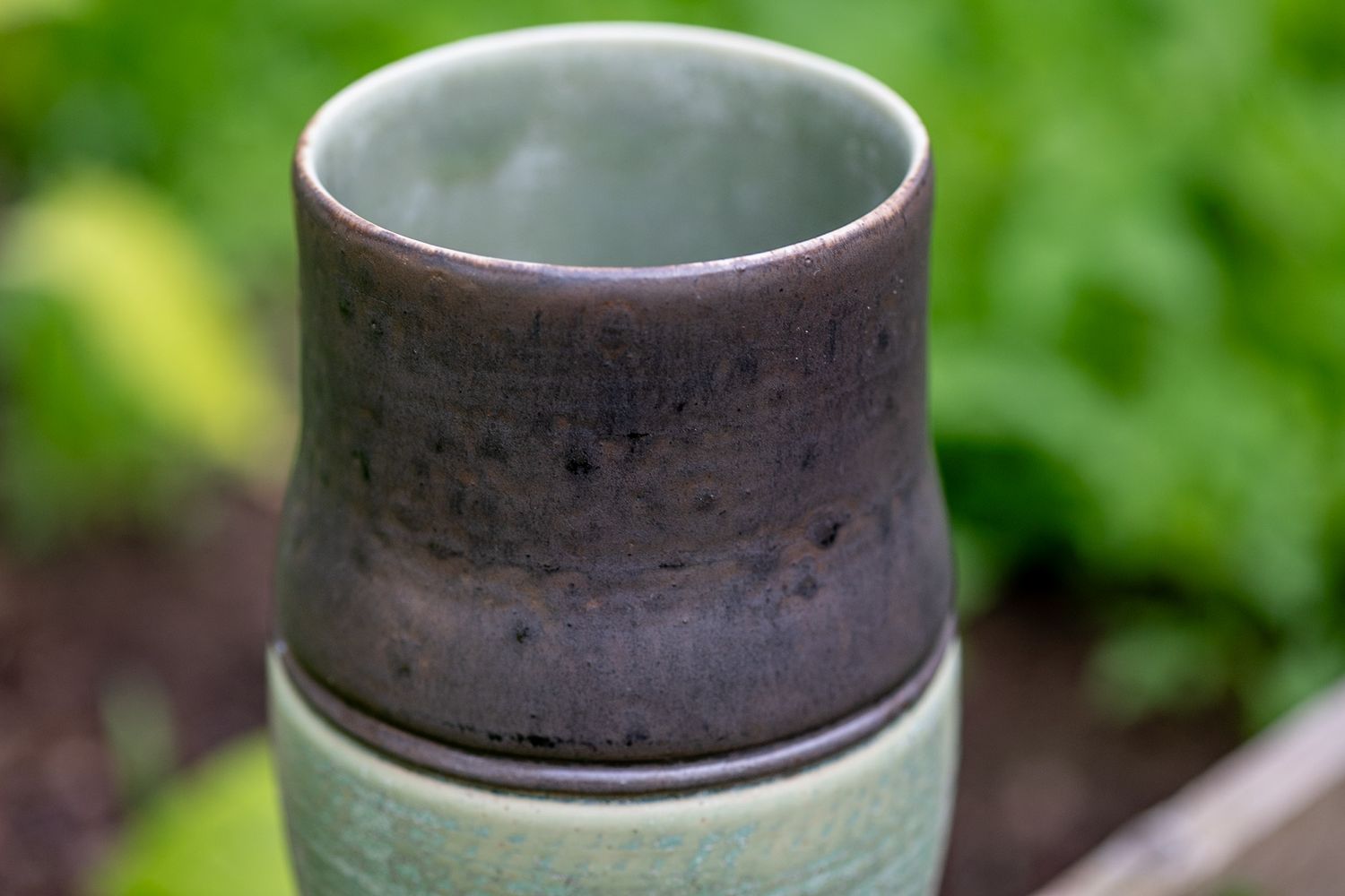 Close-up of handcrafted ceramic cup with dark brown and green glaze finish.