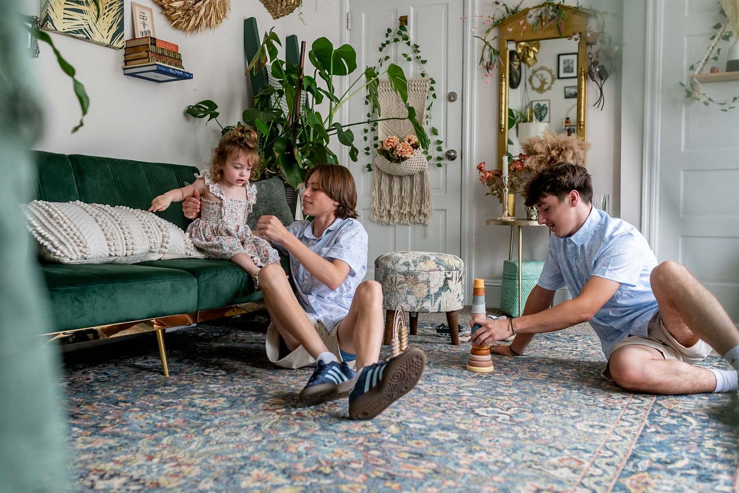 Family members sit together on a patterned rug in a bright, plant-filled room.