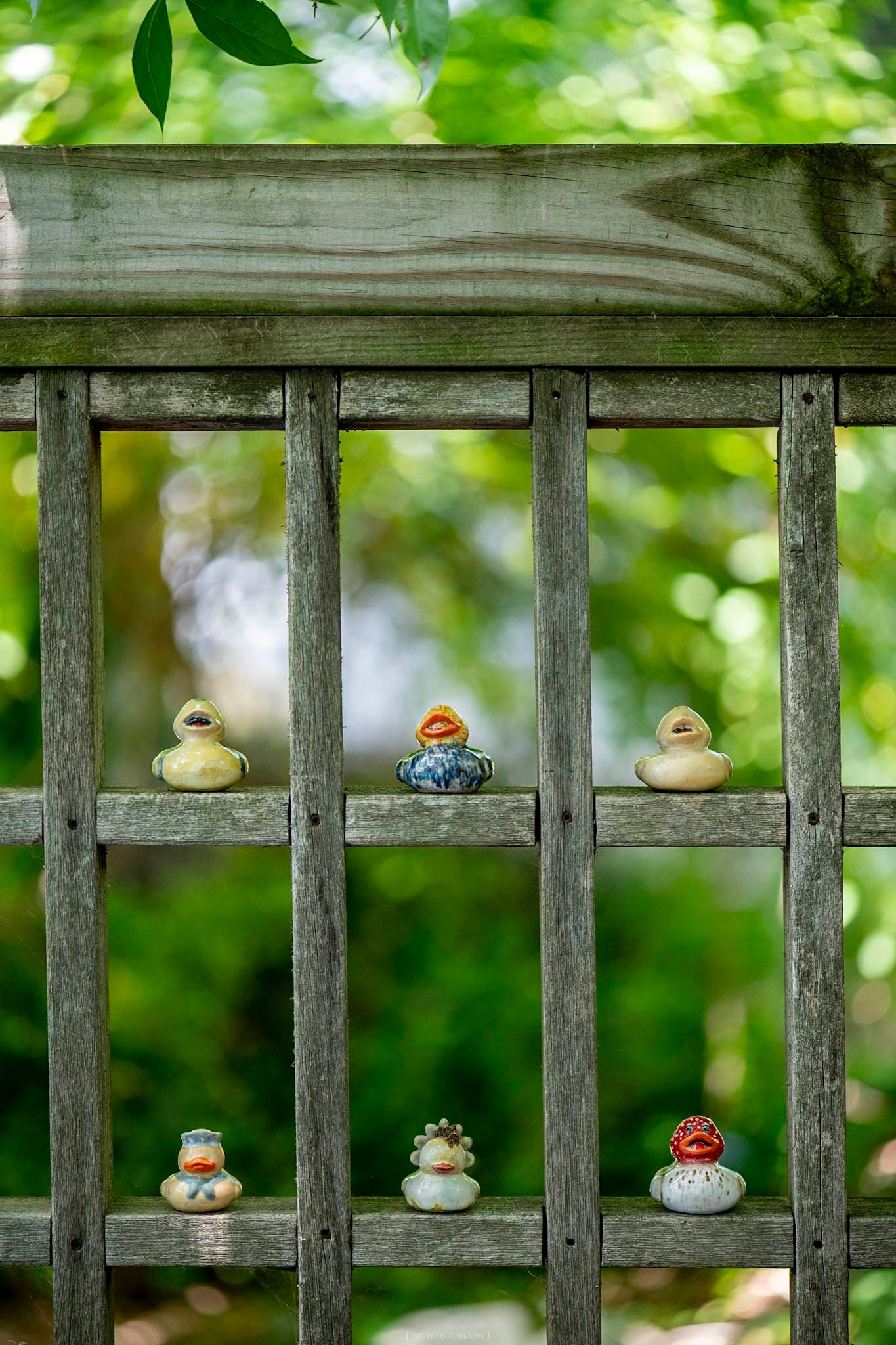 Collection of six unique handmade ceramic duck figurines displayed on a rustic wooden garden fence outdoors.