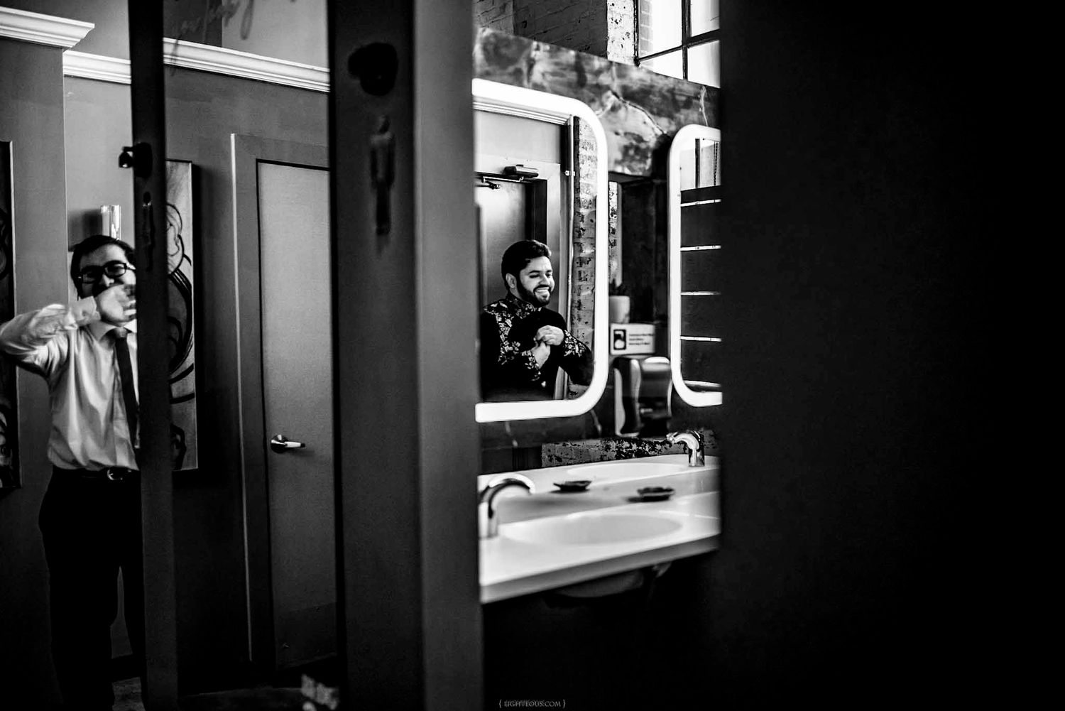 Groom preparing in bathroom mirror reflection, black and white wedding photography.