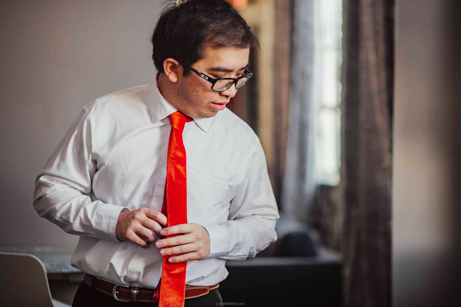Man in white dress shirt and red tie adjusting his cufflinks while getting dressed for a formal event.