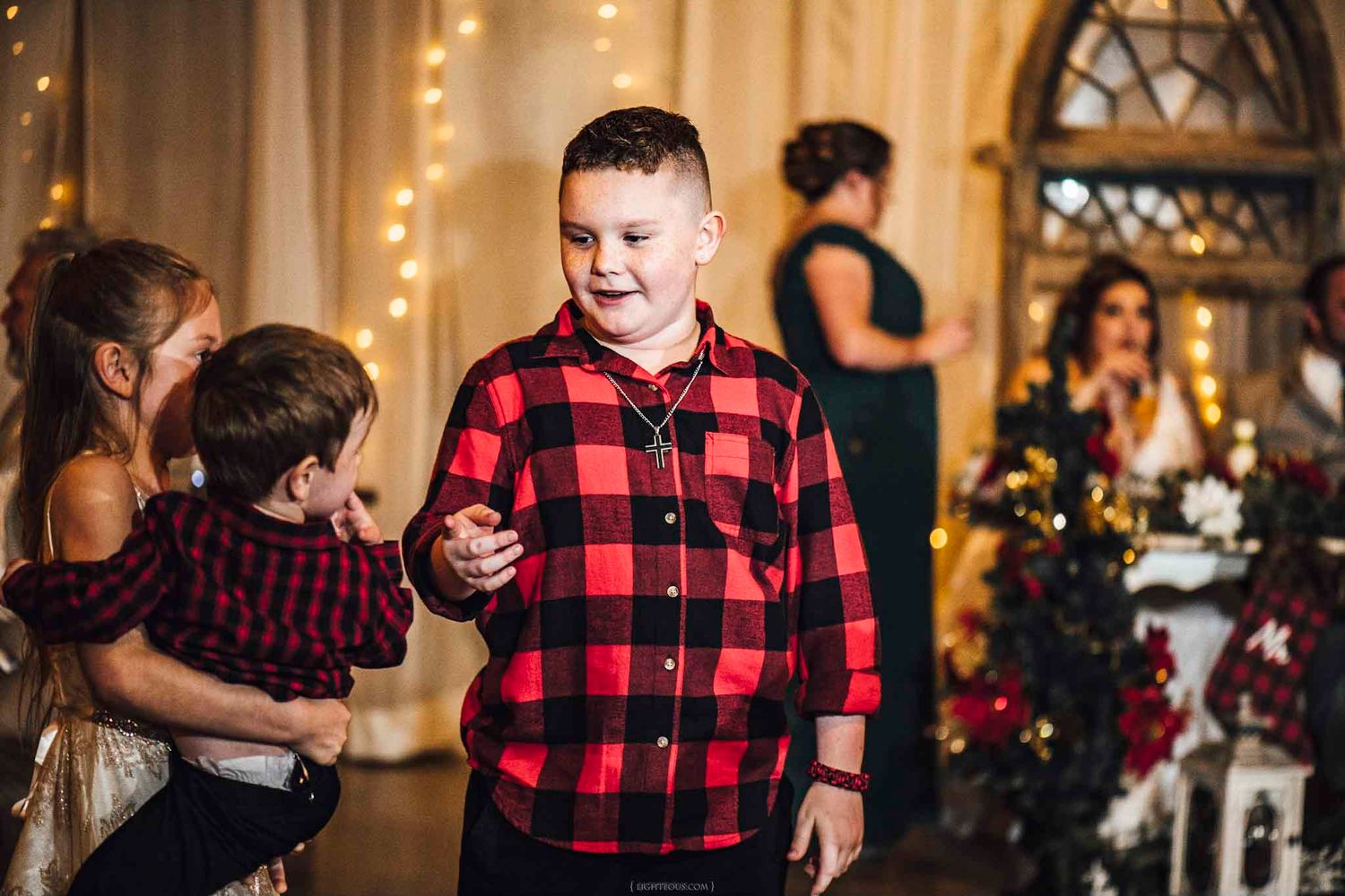 Young boy in red plaid shirt smiling at a Christmas holiday party with festive decorations.