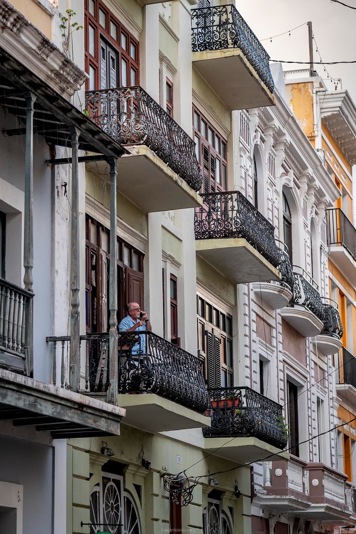 Man stands on ornate wrought iron balcony of a historic colonial building in Old San Juan, Puerto Rico.
