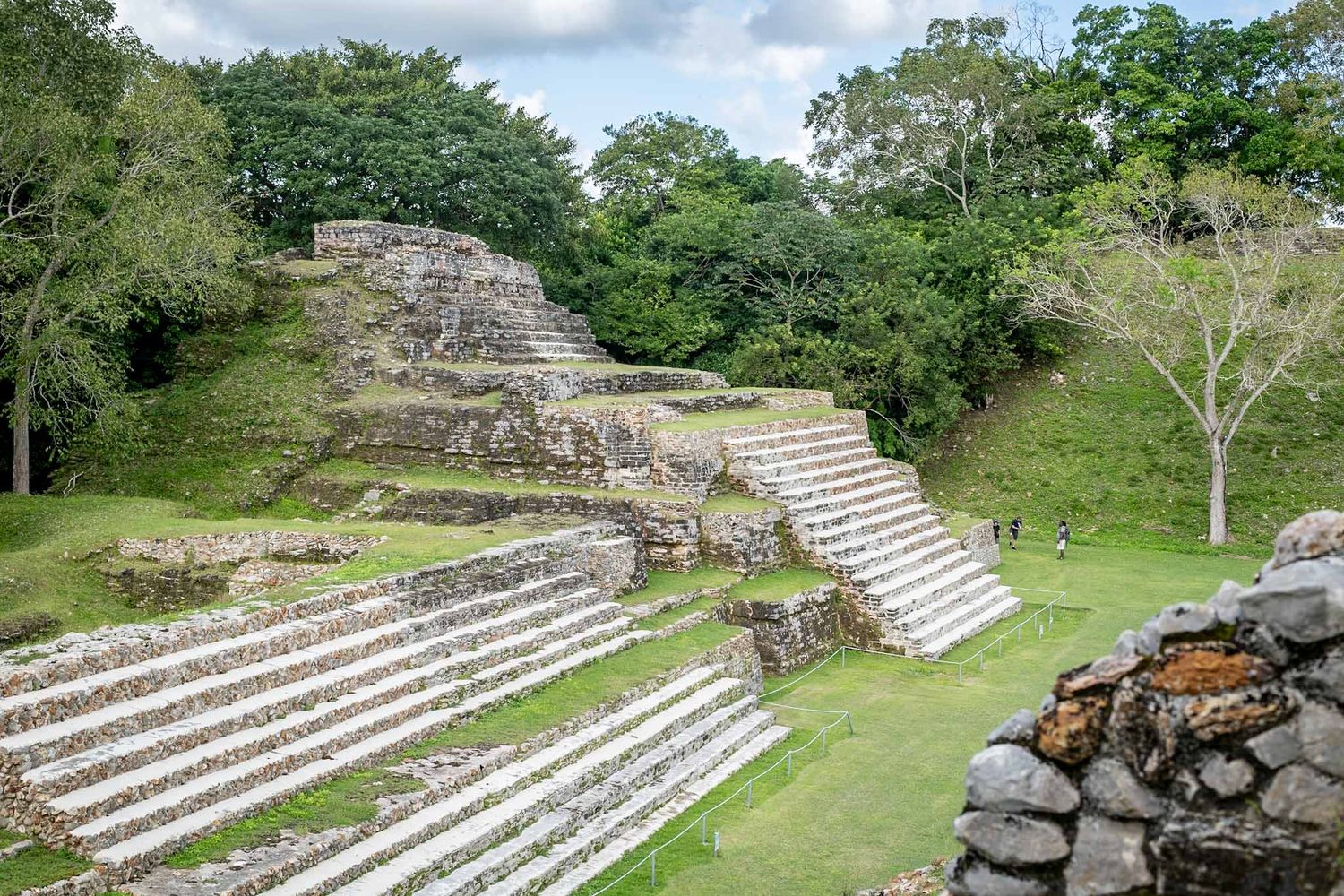 Ancient stone terraces and steps of Mayan ruins surrounded by lush green vegetation.